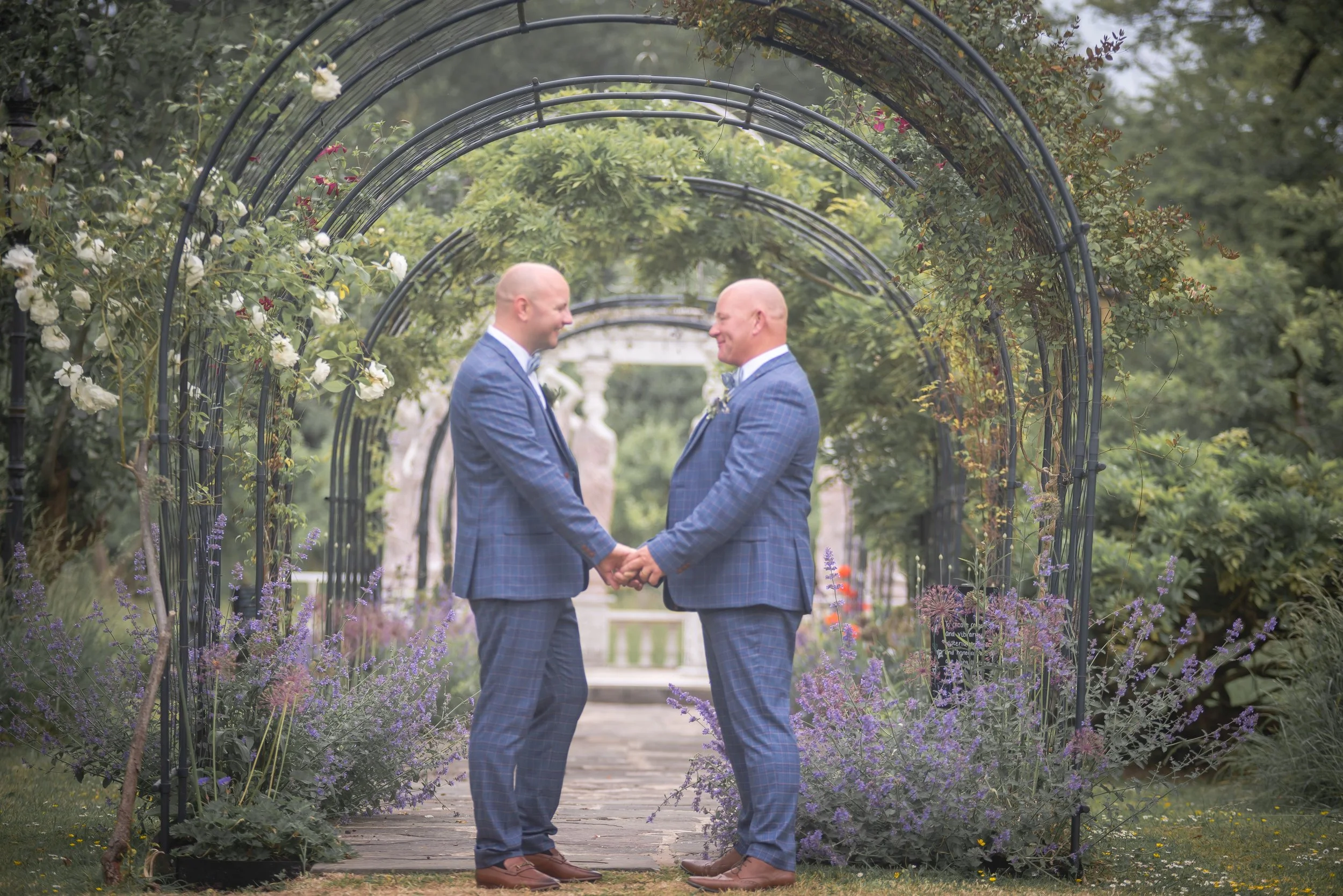 2 grooms holdings hands in secret garden at Berwick Lodge