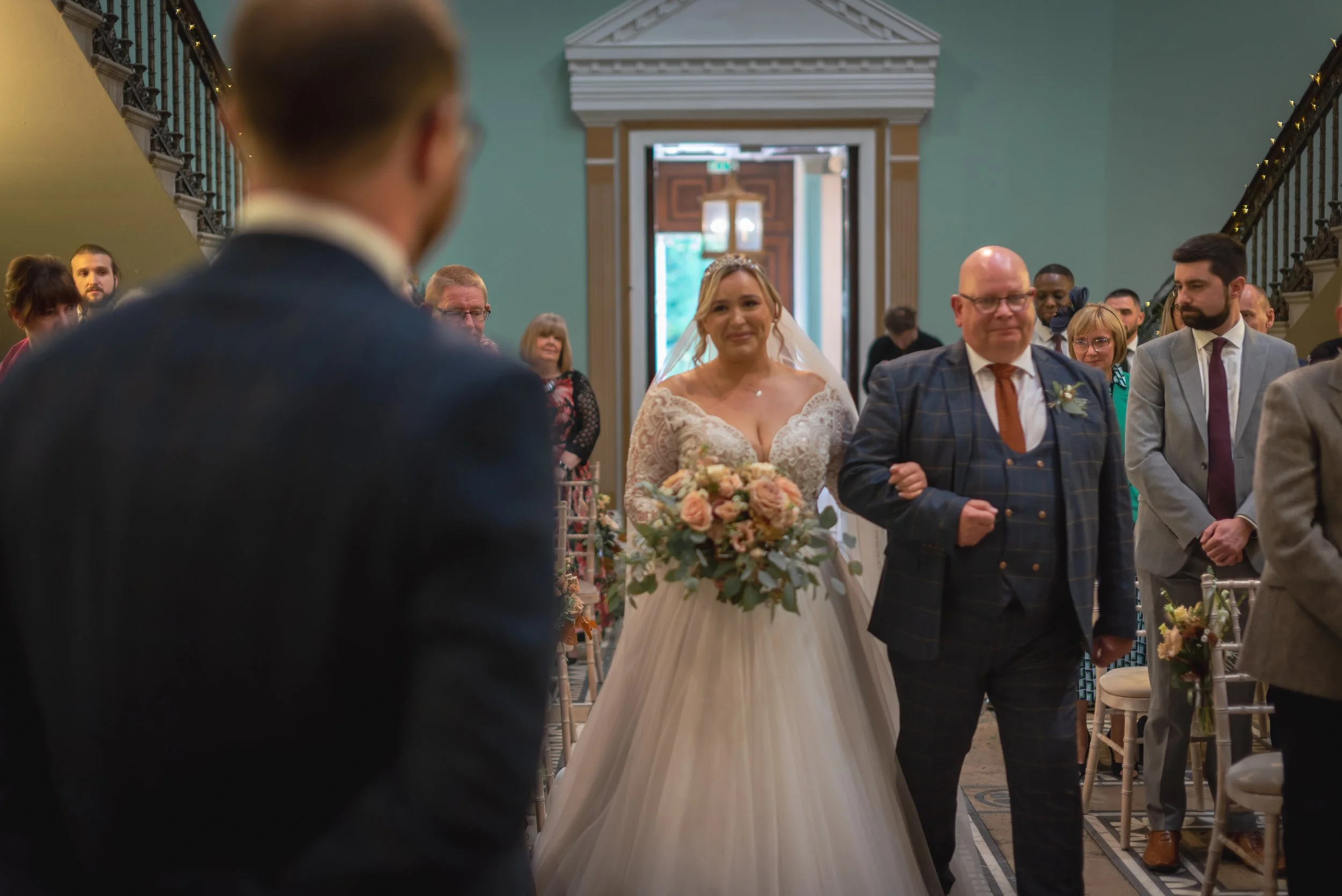 A bride walking down the aisle with her father at a wedding ceremony, surrounded by seated guests at Leigh Court taken by Leigh Court preferred wedding photographer.