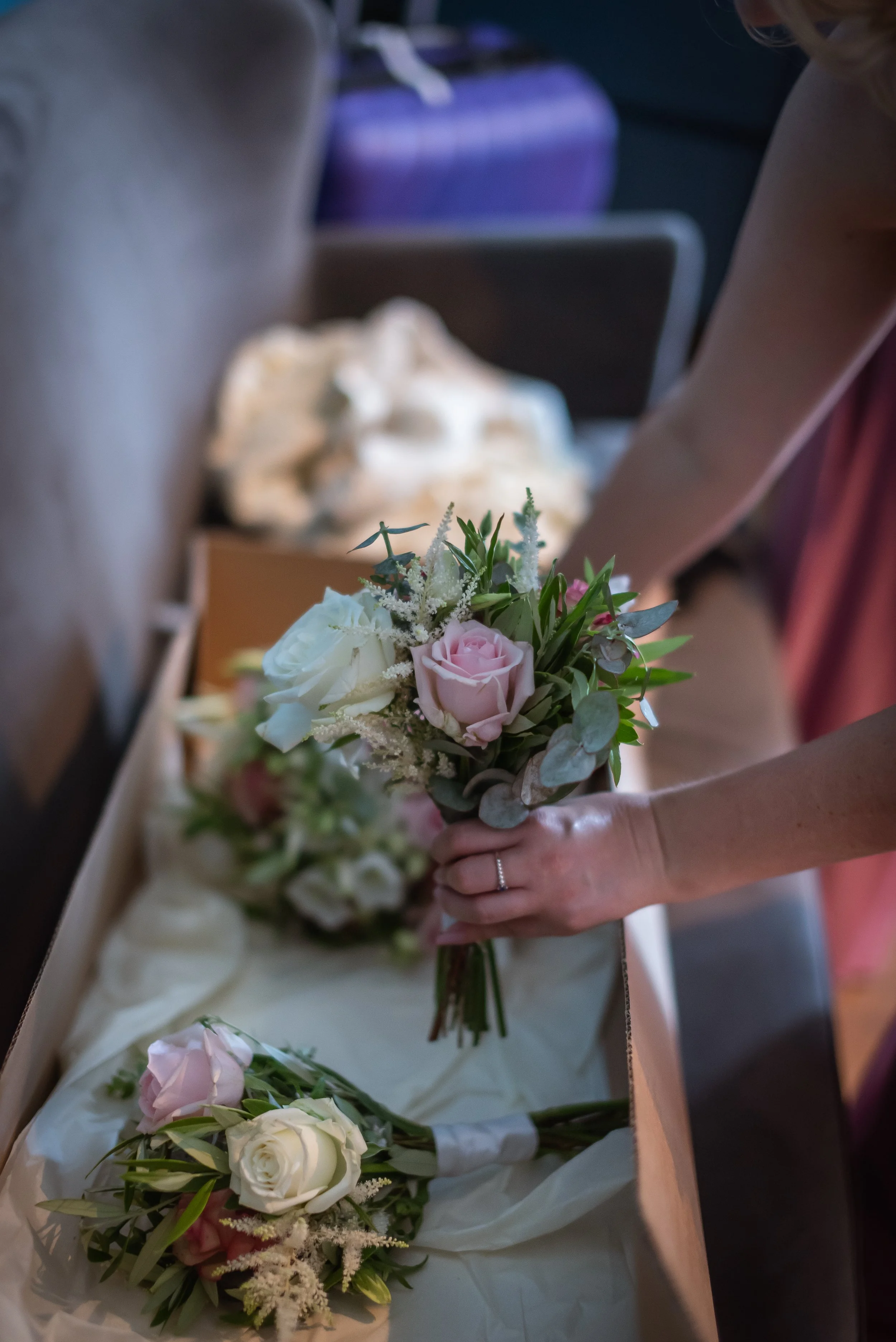 Person holding a bouquet of pink and white roses with green foliage, preparing flowers on a table with other flower arrangements for a special occasion snapped by a Wedding Photographer in Bristol.