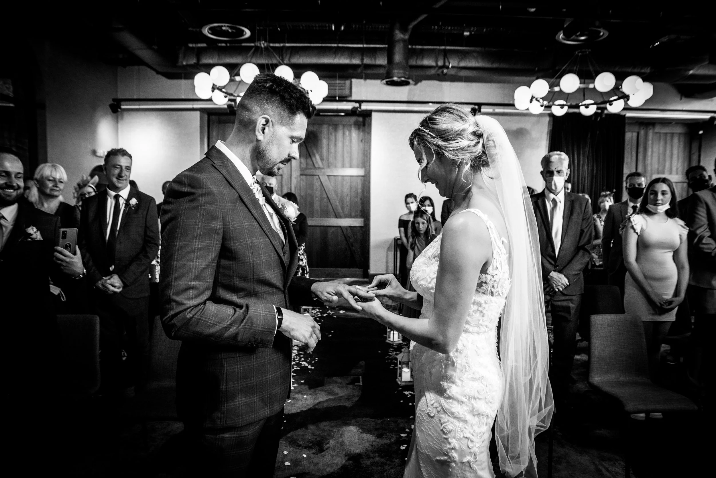 A black and white photo of a wedding ceremony with a bride and groom exchanging rings, surrounded by guests in a decorated Avon Gorge Hotel in Cifton