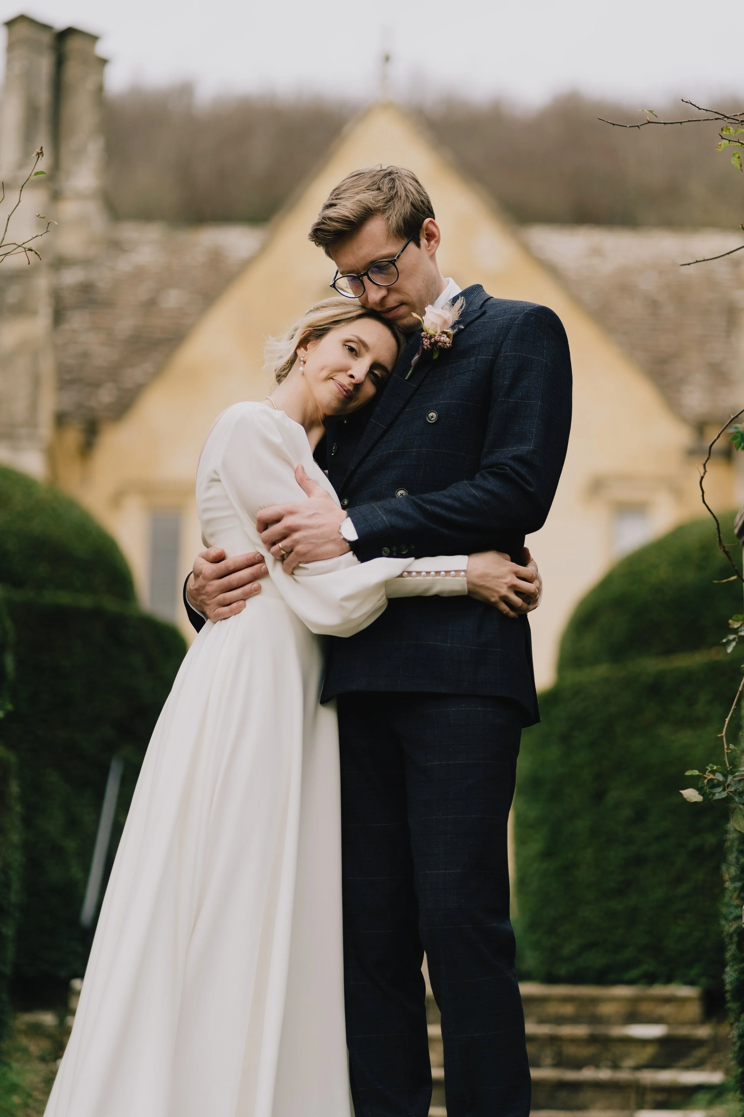 Bride and Groom holding each other in front of Owlpen Manor captured by Bristol Wedding Photographer