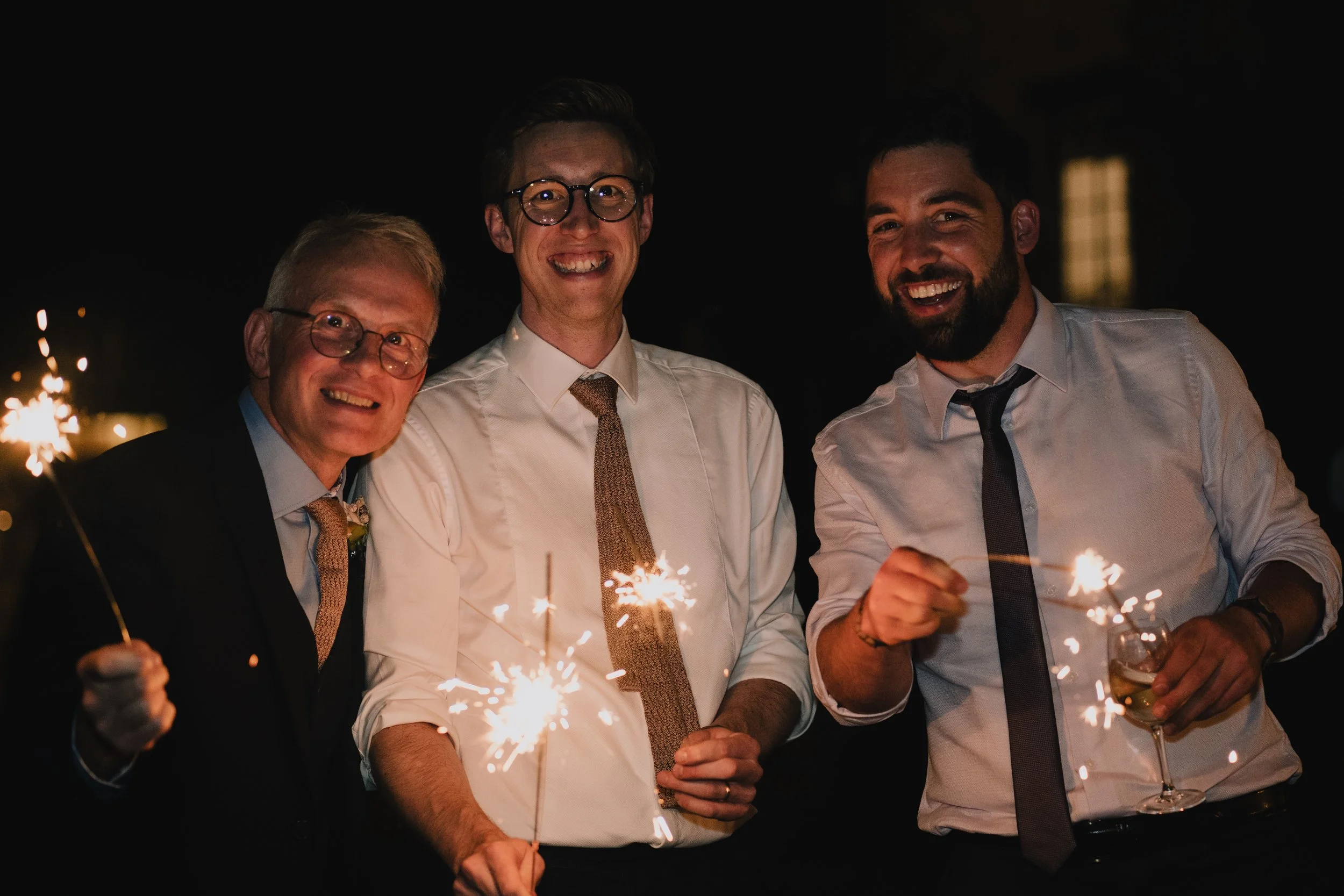 Groom celebrating with sparklers surrounded by wedding guests during evening reception