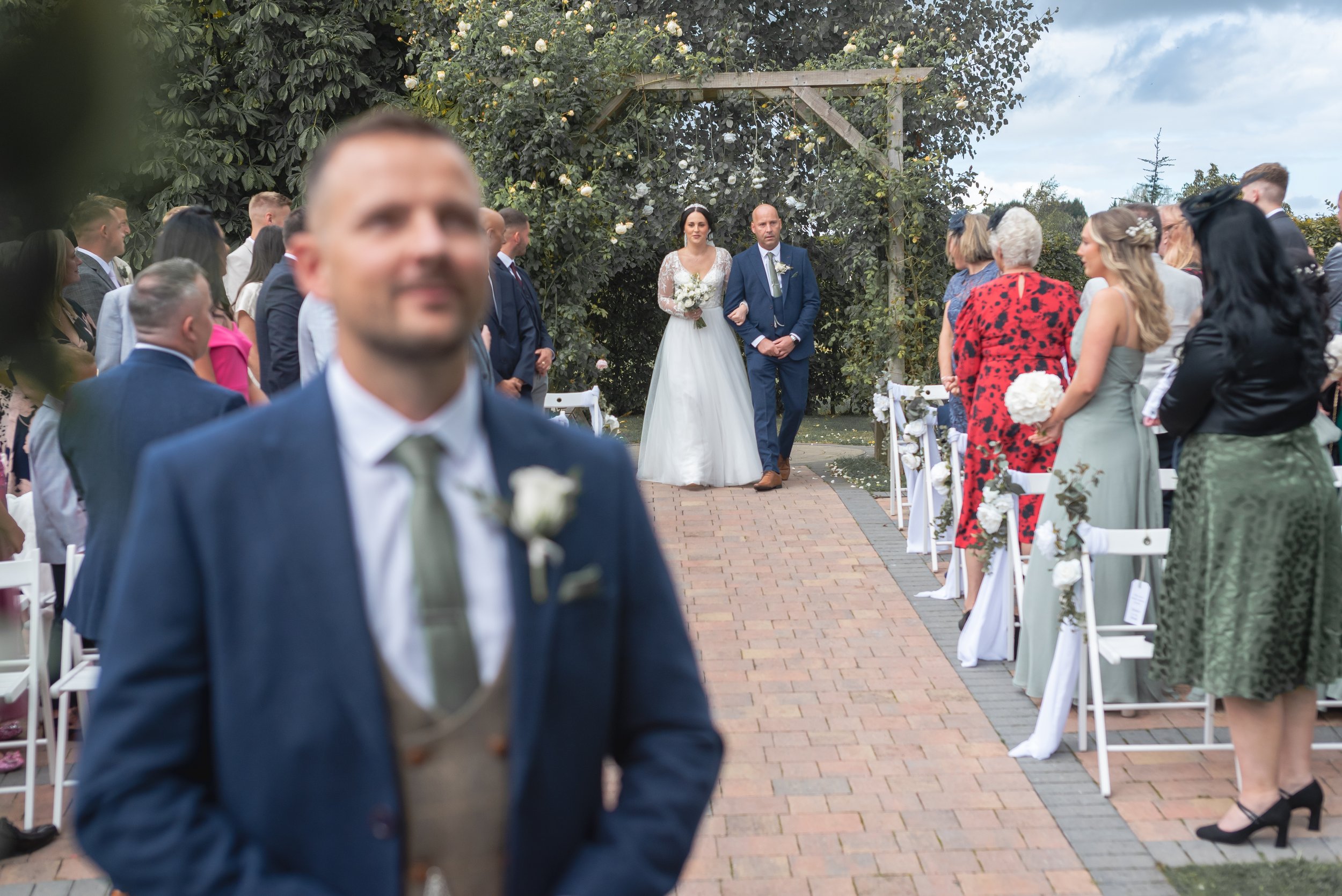 A bride and groom walking down the aisle at their outdoor wedding ceremony with guests on either side watching at Wootton Park in Midlands