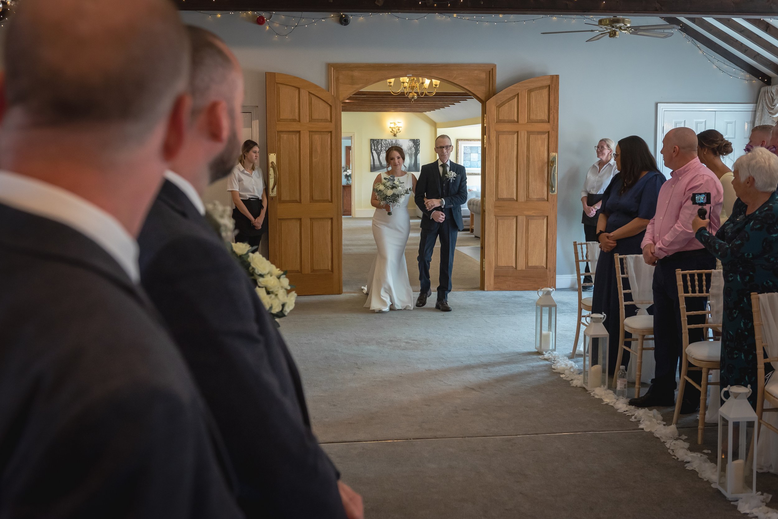 Bride walking up the aisle with her father as guests and groom look on in happiness