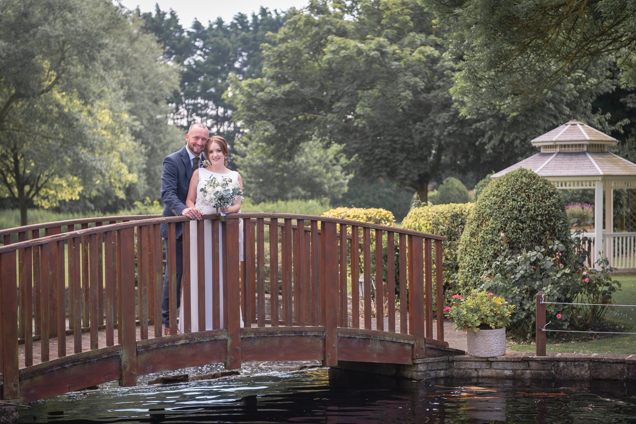 Bride and Groom standing on bridge at Batch Country House smiling with sun setting behind them