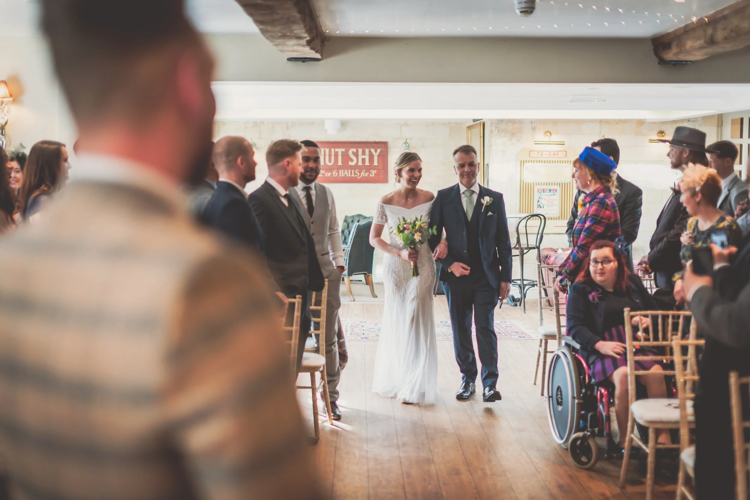 Bride and groom walking down the aisle at their wedding ceremony, surrounded by seated guests and friends in a rustic indoor venue at Moonraker Hotel in Braadford on Avon