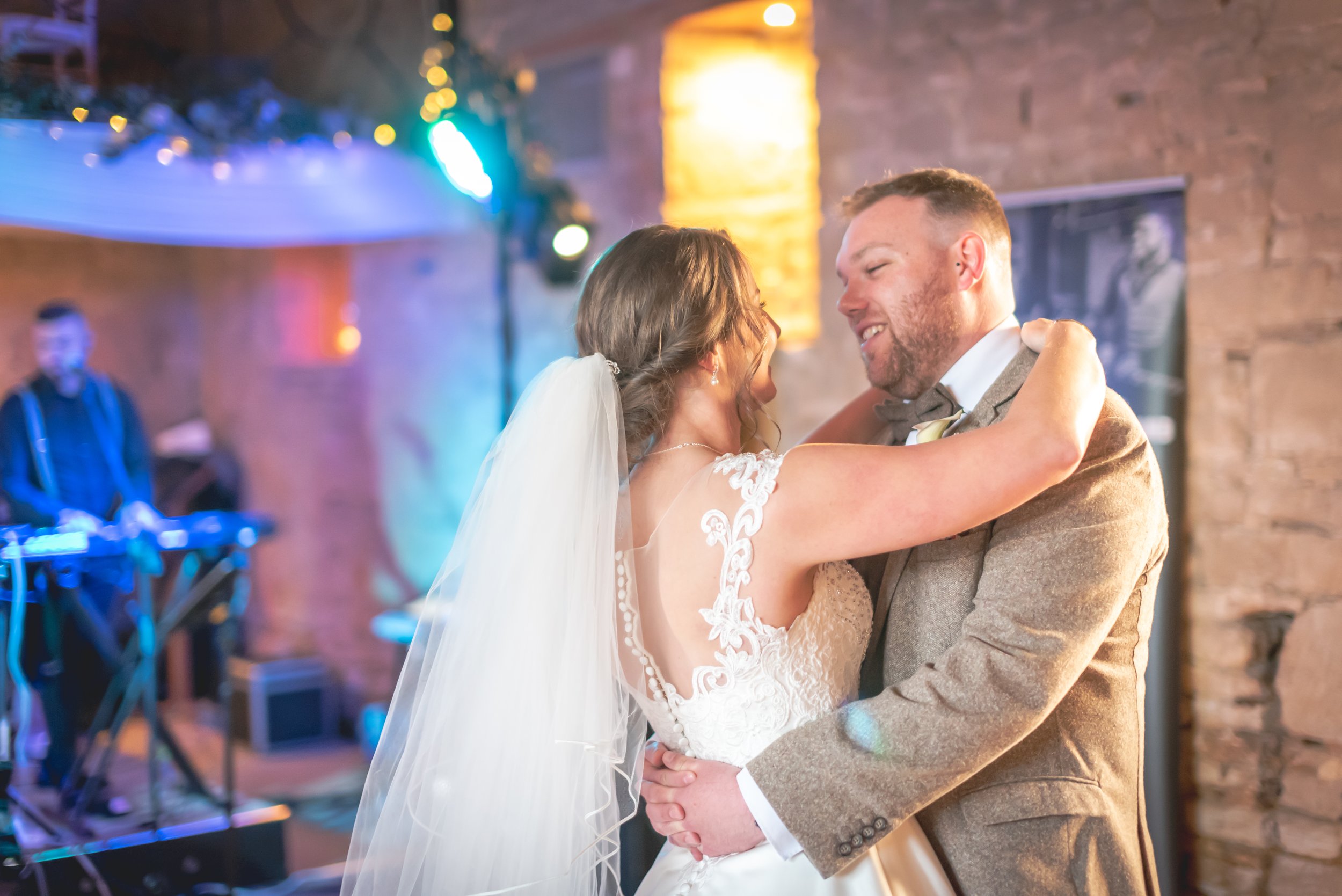 A bride and groom dancing closely at their wedding reception, with the bride wearing a lace wedding dress and veil, and the groom in a beige suit with a bow tie during the first dance taken by Great Tythe Barn Wedding Photographer.