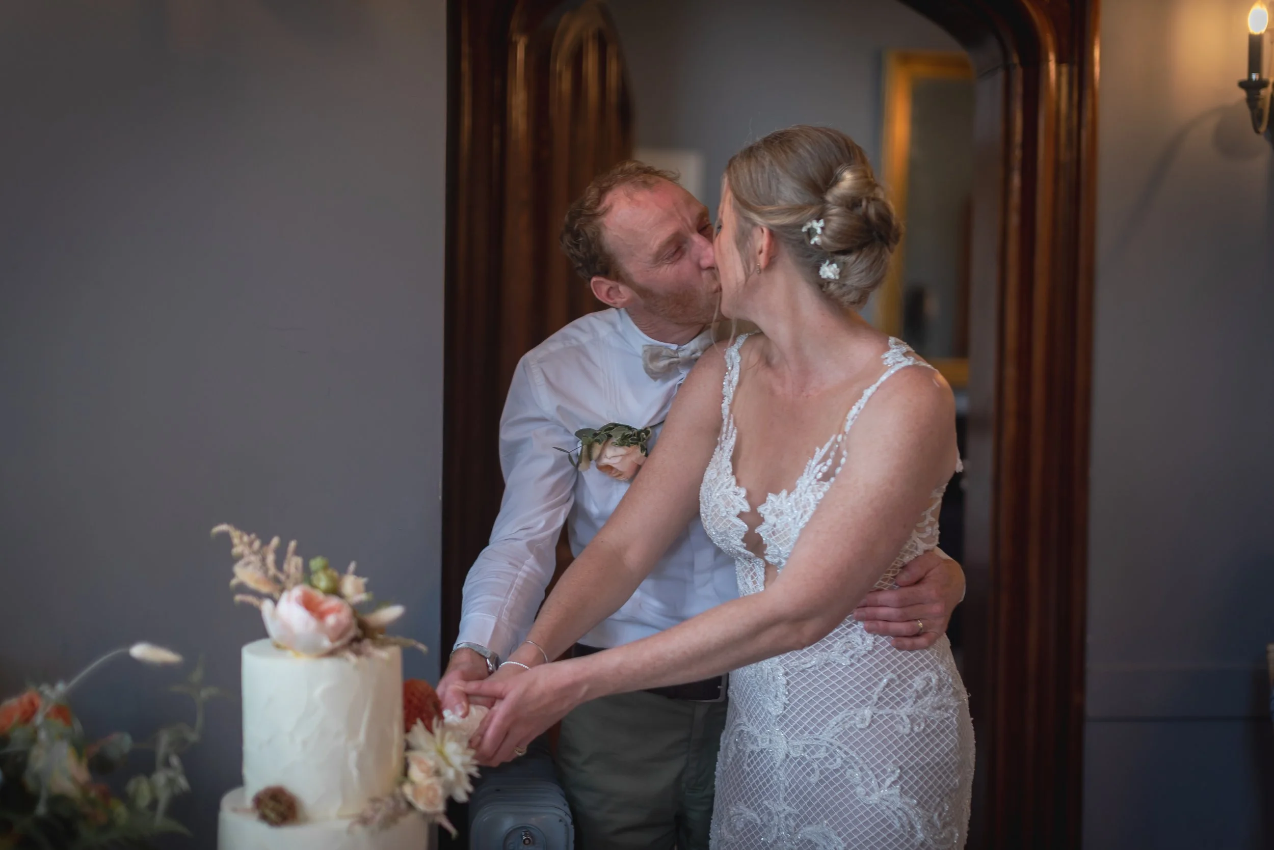 A bride and groom share a kiss in front of a wedding cake with flowers during their wedding celebration at the now derelict DIllington House