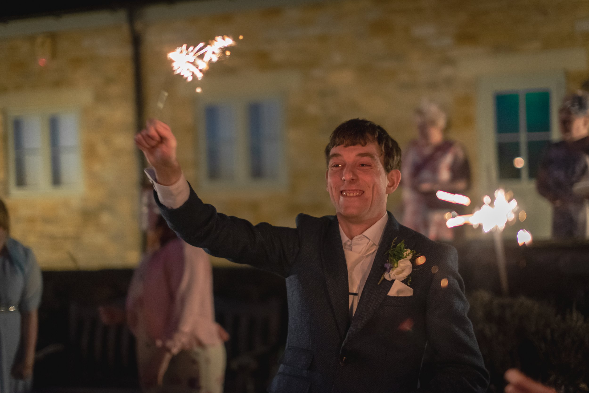The groom proudly waving a sparkler after an incredible wedding day at Deer Park Hall in Cotswolds