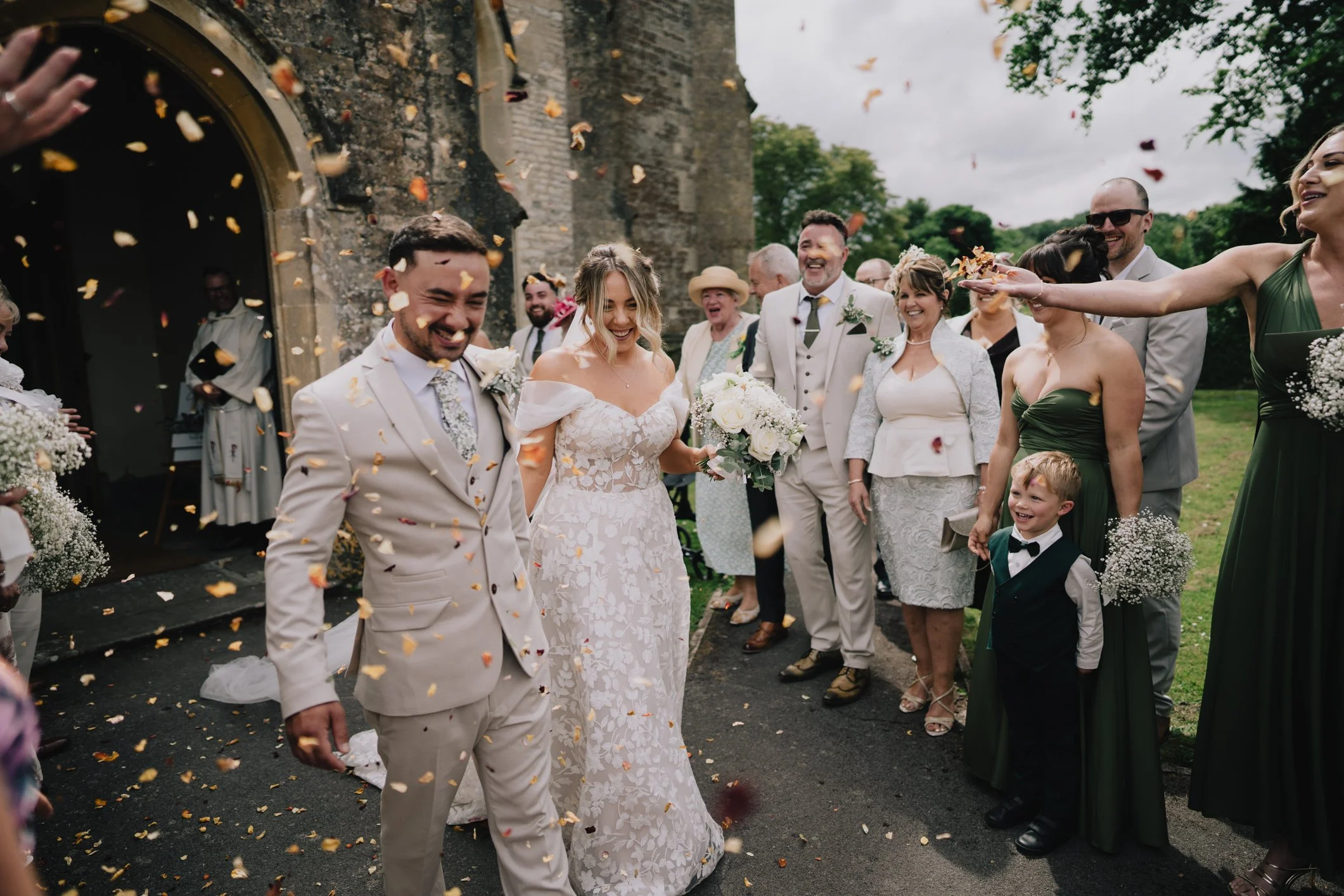 Joyful confetti moment outside St John’s Church Radstock with bride and groom laughing surrounded by guests