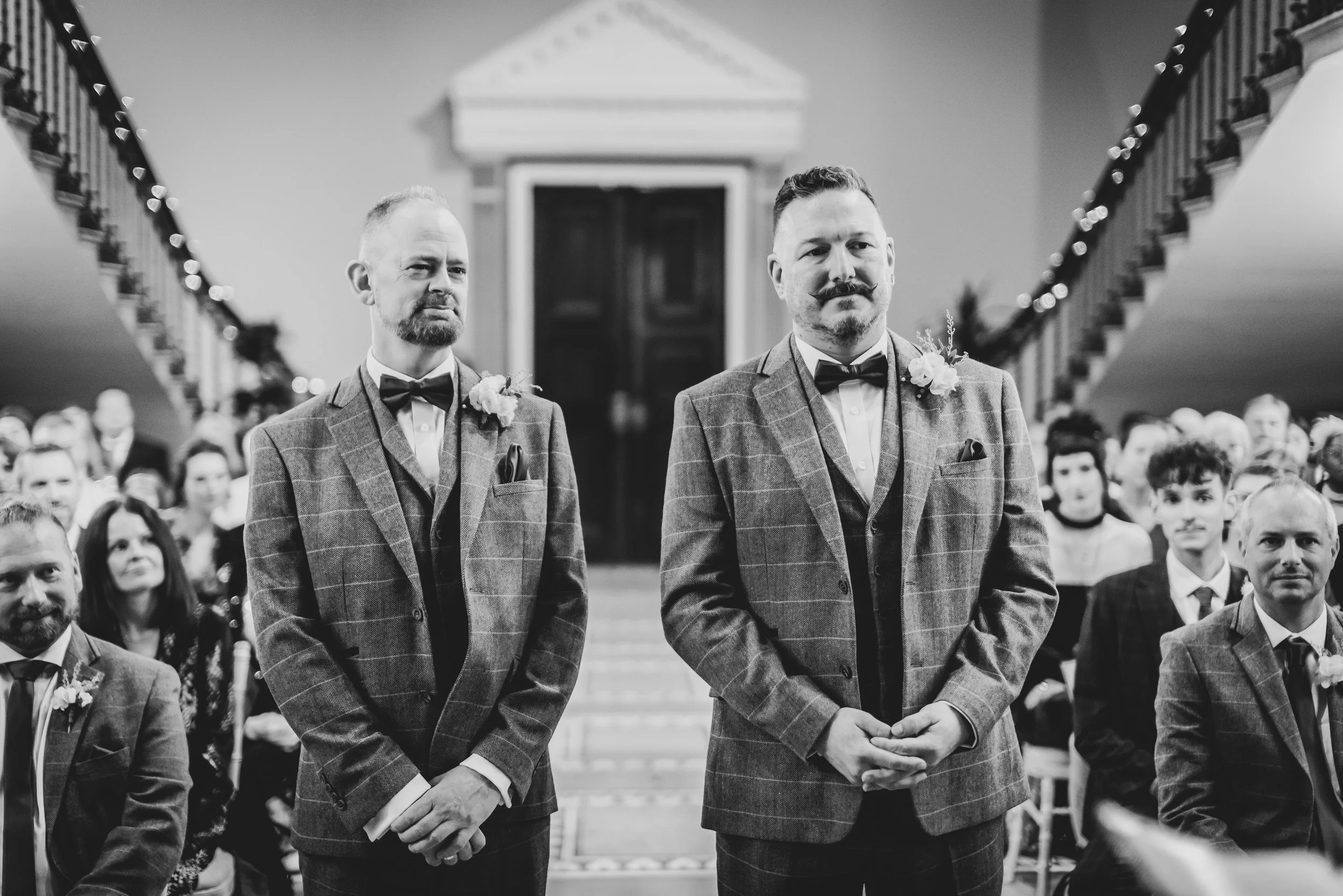 Black and white photo of Andy and Issac standing together at the top of the aisle, moments before exchanging vows.