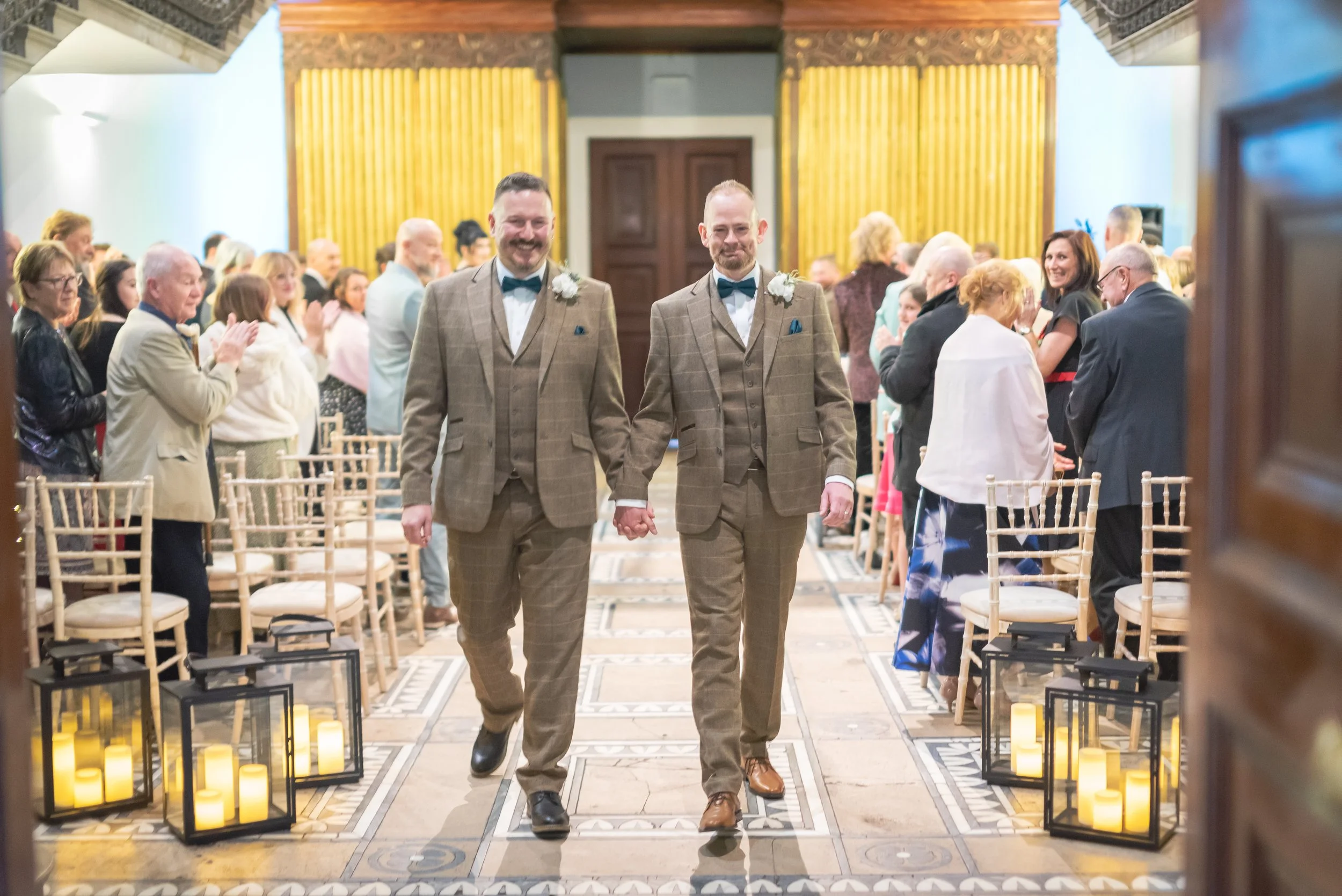 Andy and Issac walking hand in hand down the aisle as newlyweds, with smiles and applause all around.