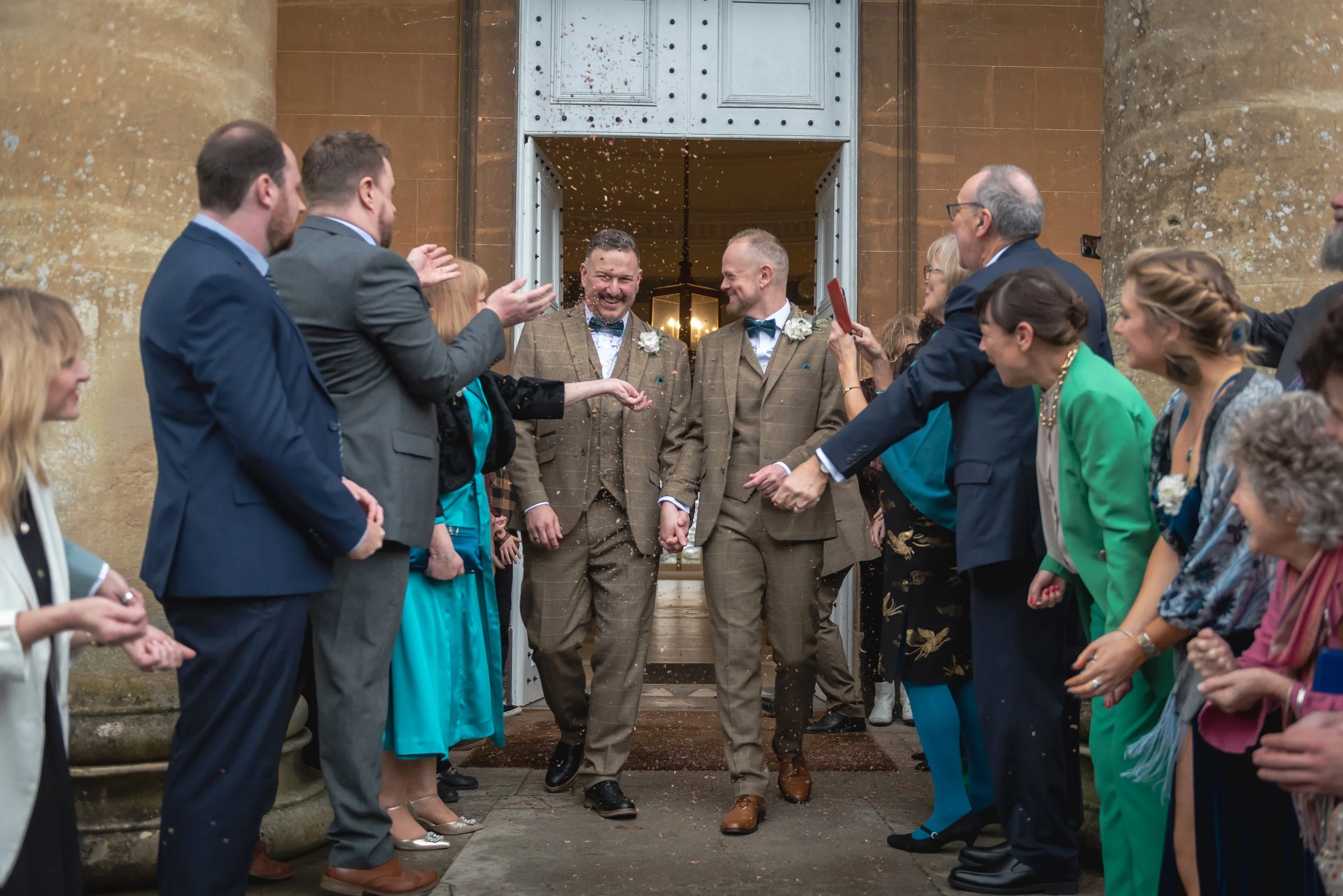 Andy and Issac stepping out of Leigh Court as guests throw colourful confetti to celebrate their marriage.