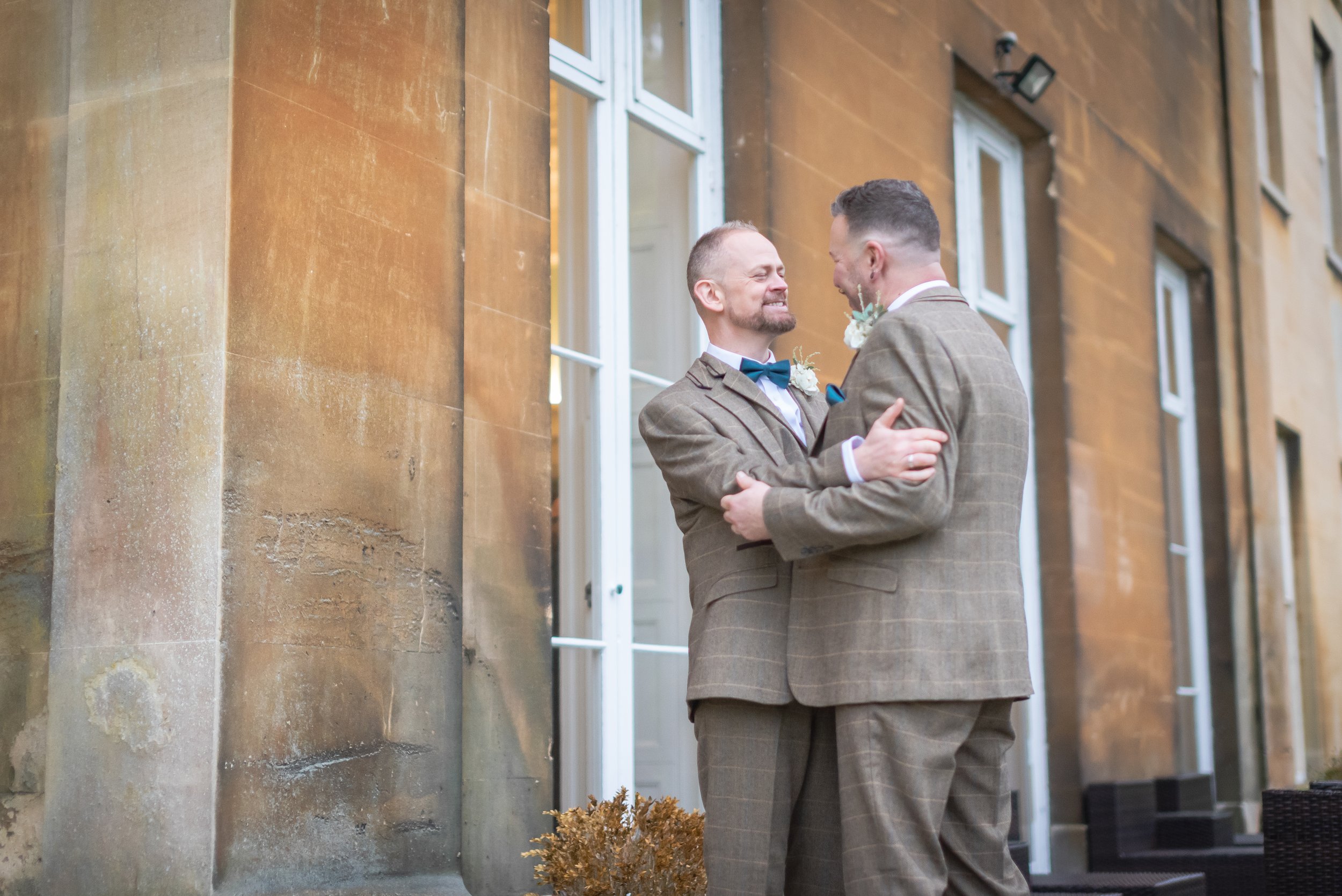 Intimate moment of Andy and Issac hugging and gazing at each other lovingly outside the grand entrance of Leigh Court.