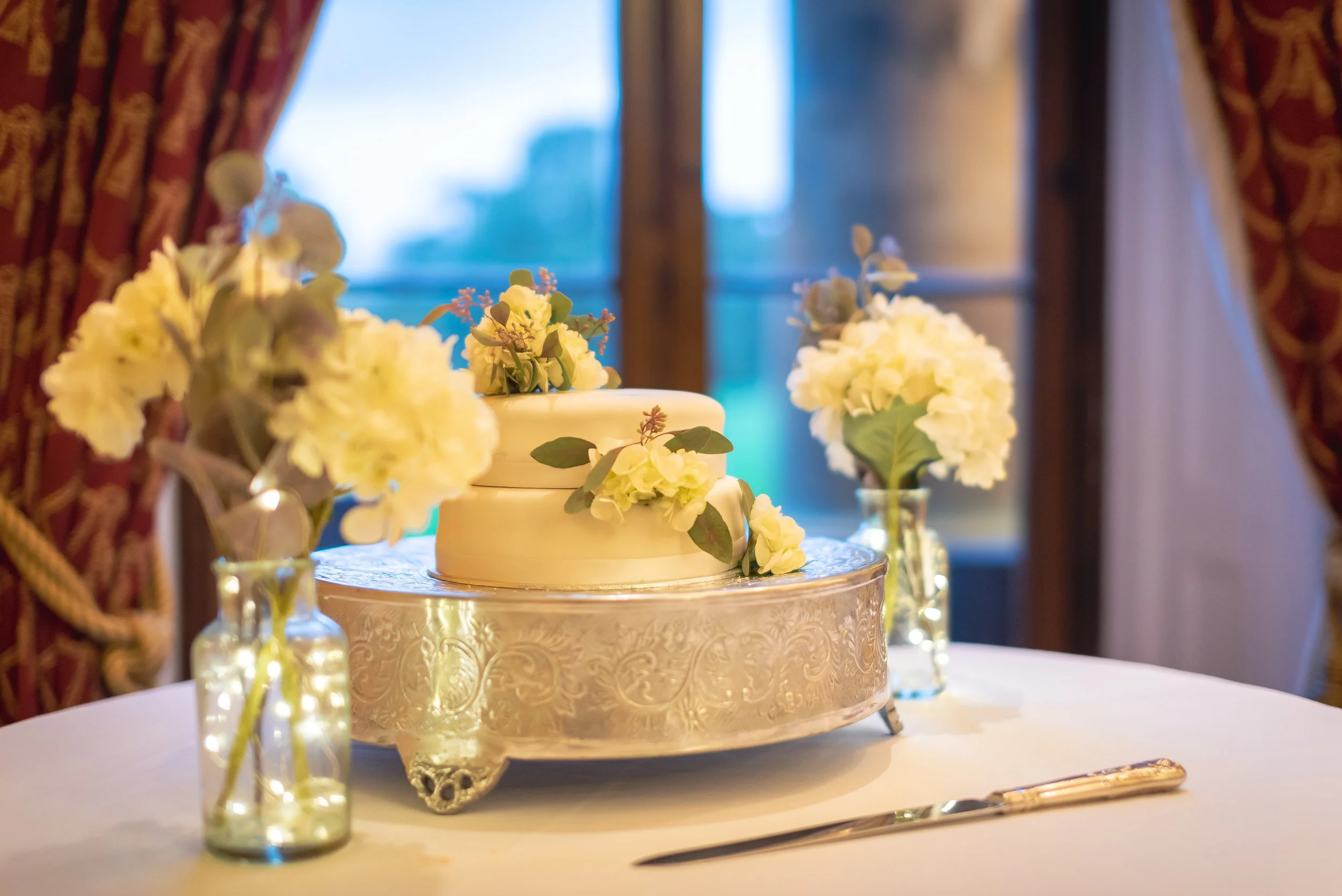 Elegant wedding cake adorned with fresh flowers, displayed in front of a classic Leigh Court backdrop.