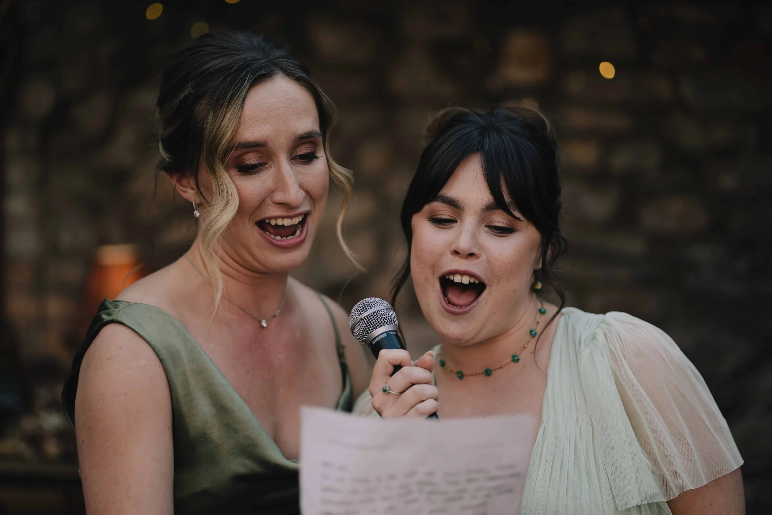 Two women singing into a microphone and reading from a paper during weding reception at Radnor Rooms, Bristol.