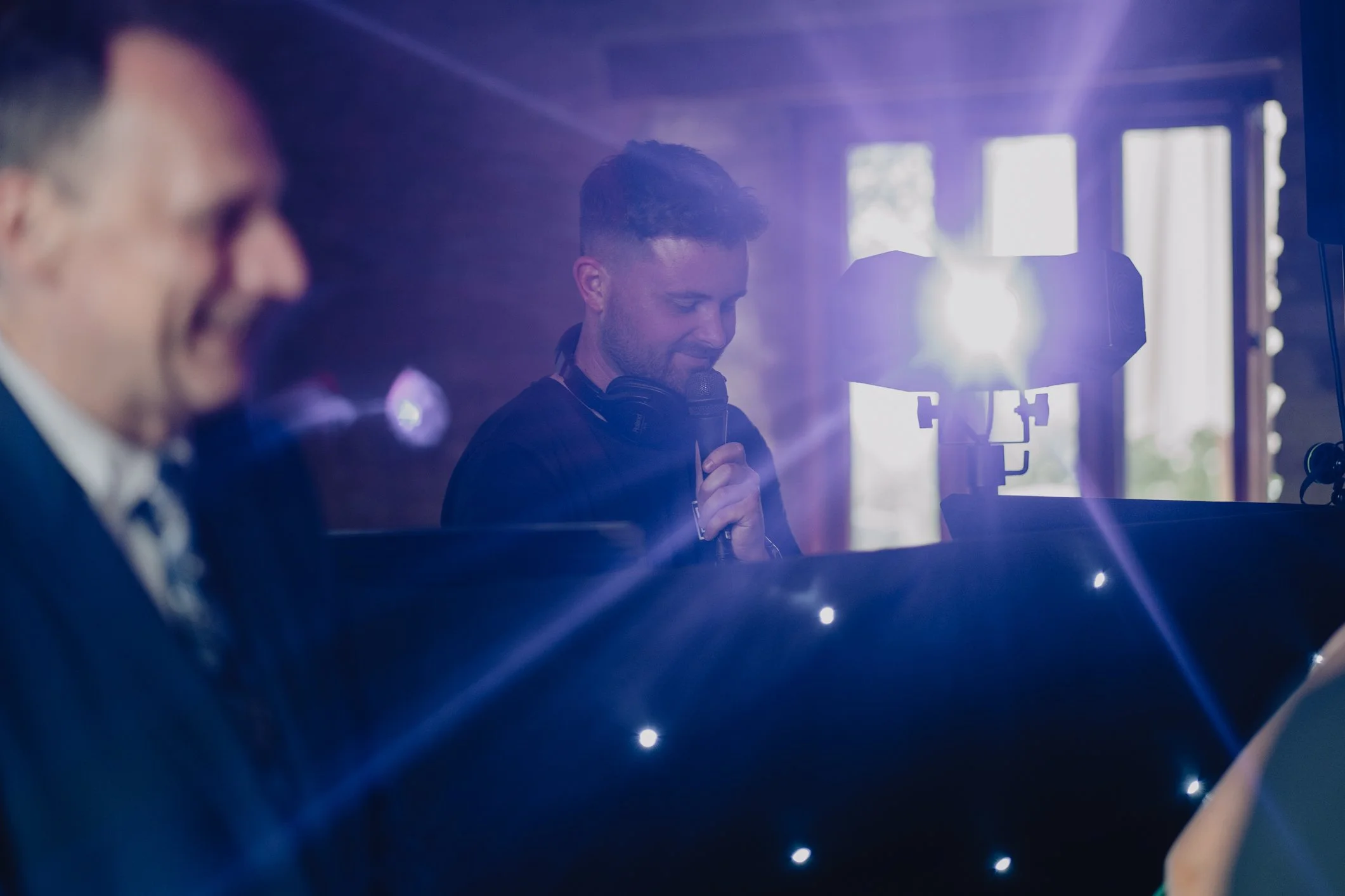 Man singing into a microphone at a piano during a performance with blue lighting.