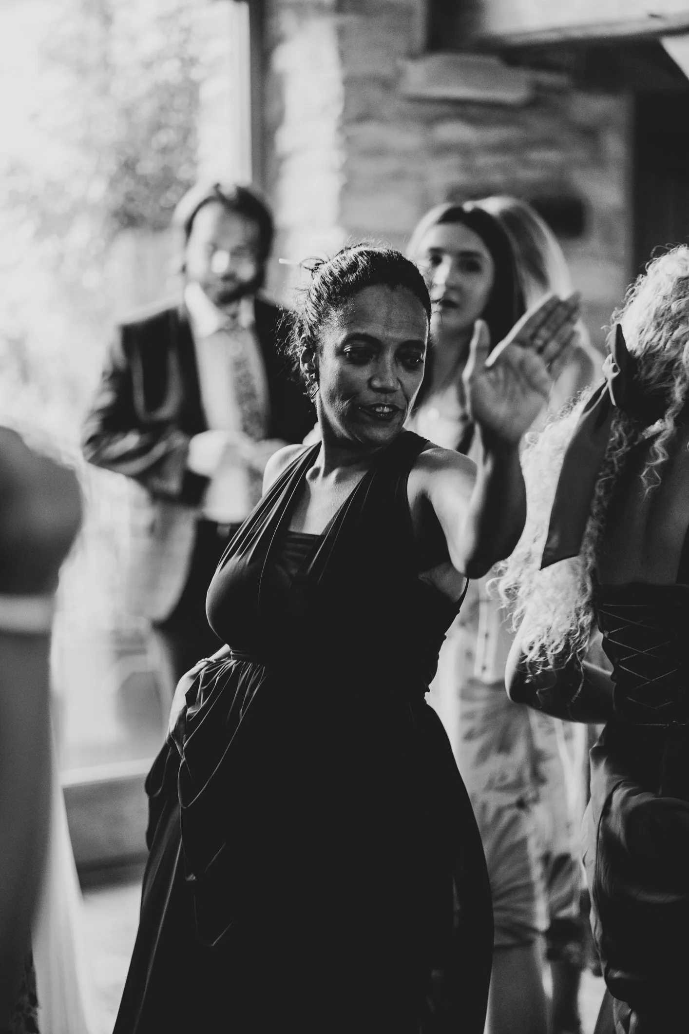 A woman in a black dress dancing at a social gathering, with other people in the background, in a black and white photo.