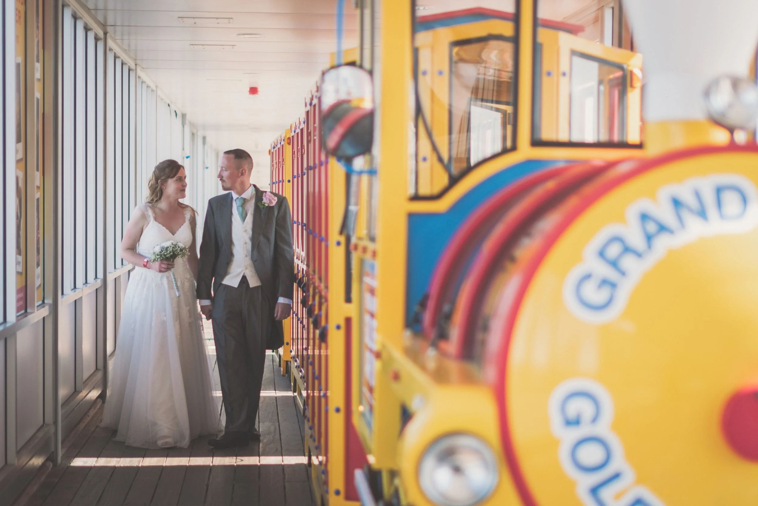 A bride and groom dressed in wedding attire, holding hands and walking down the waist at a Grand Pier Wedding in Weston-super-Mare