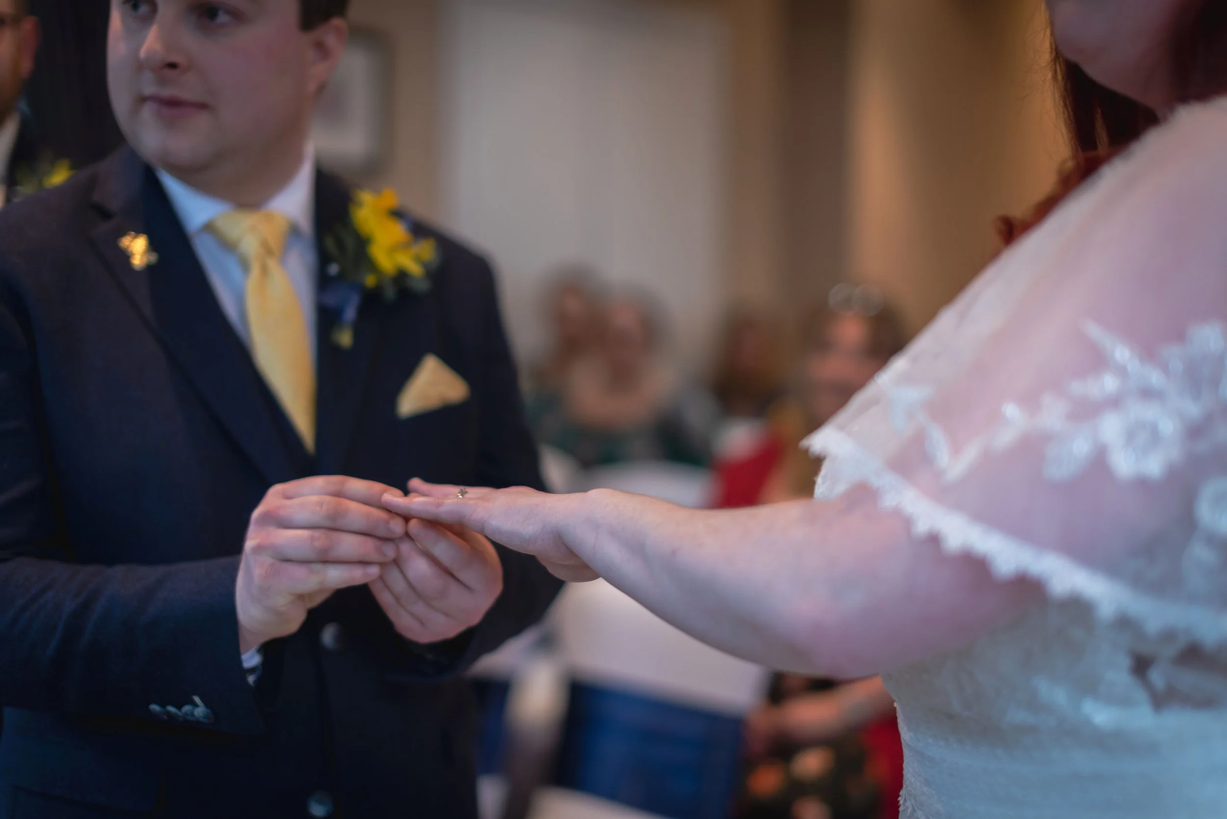 A couple exchanging wedding rings during a wedding ceremony, with guests seated in the background captured by Midland wedding photographer.