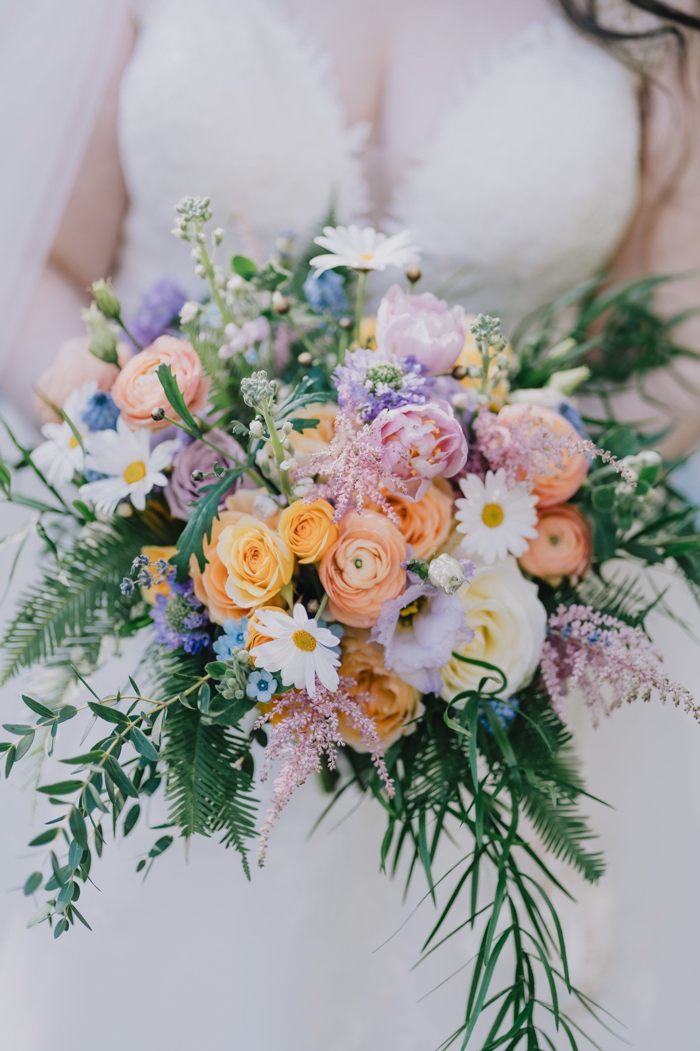 Close-up of a colorful flower bouquet with roses, daisies, peonies, and greenery.