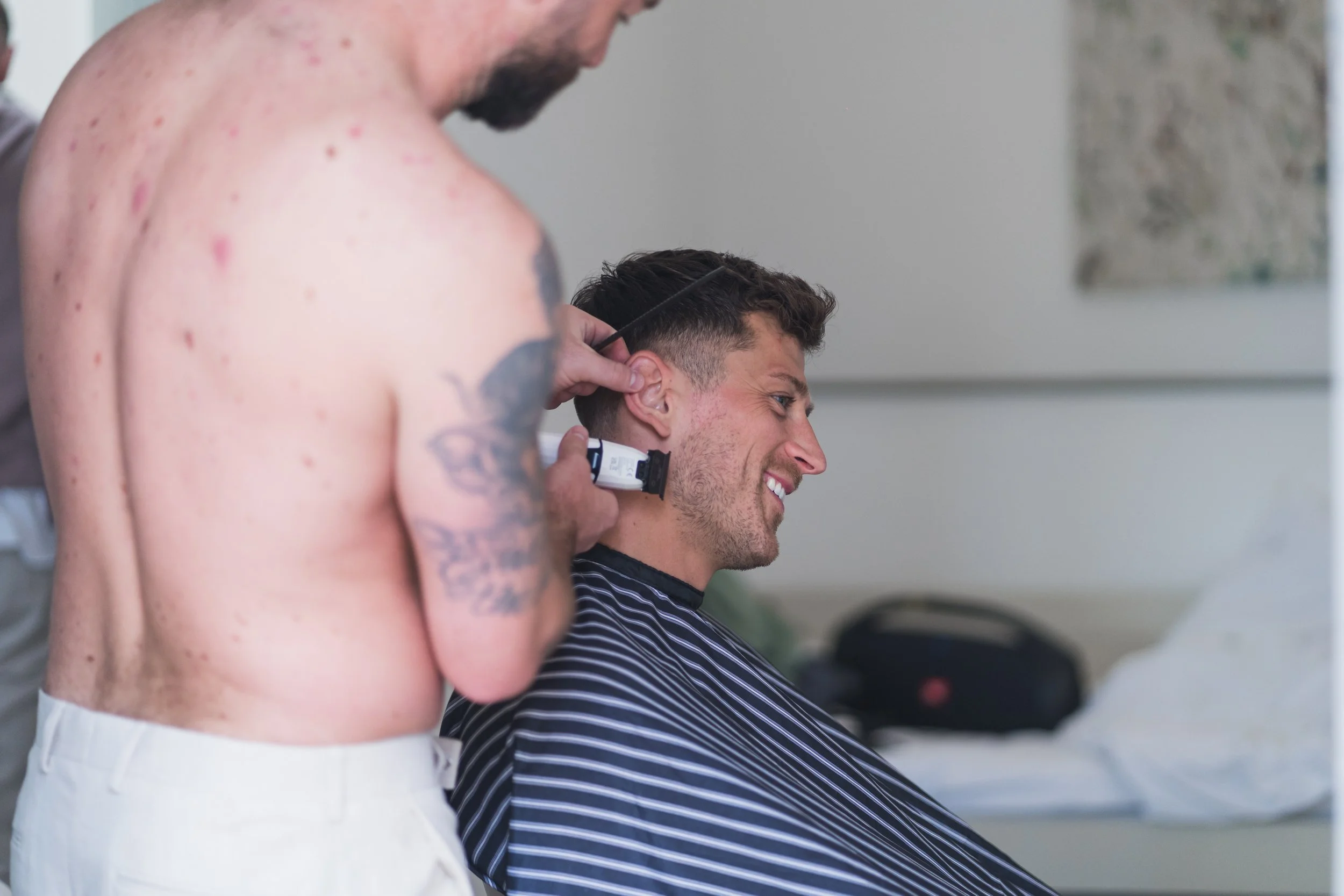 Barber trimming a young man's hair in a barbershop, with the man smiling.