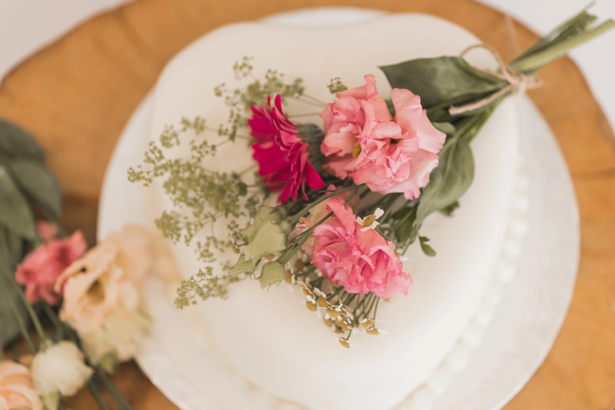 Close-up of a wedding cake decorated with pink roses, greenery, and small white flowers, with a gold-colored cake topper on top.