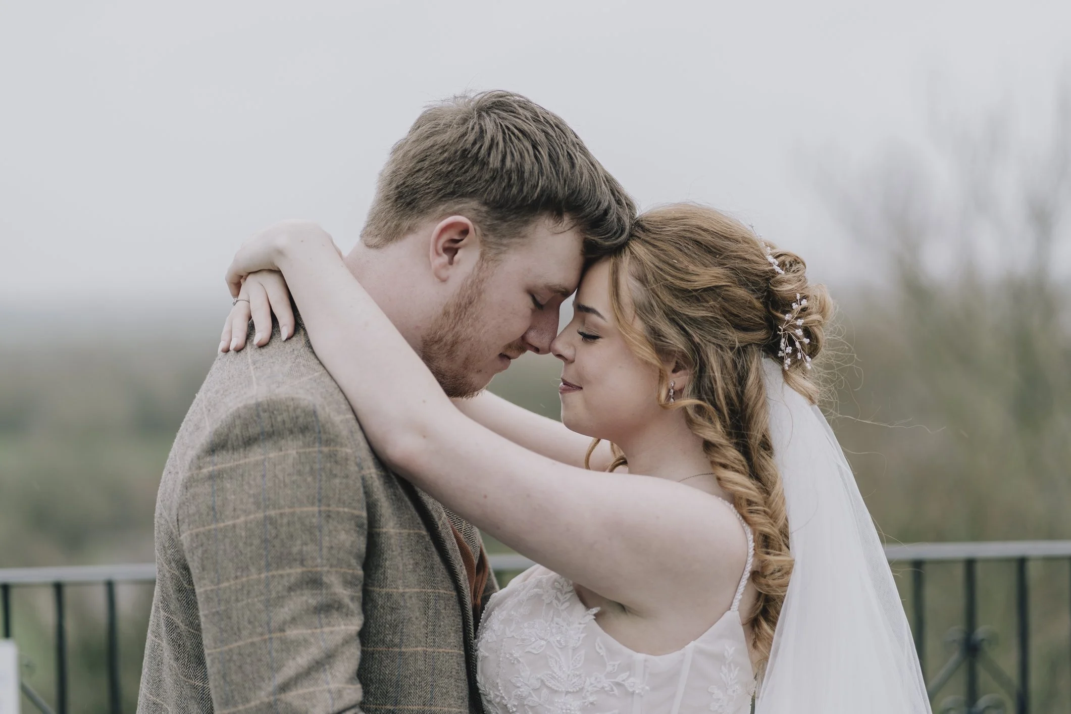 A bride and groom embracing with foreheads touching, outdoors on a cloudy day at Webbington Hotel