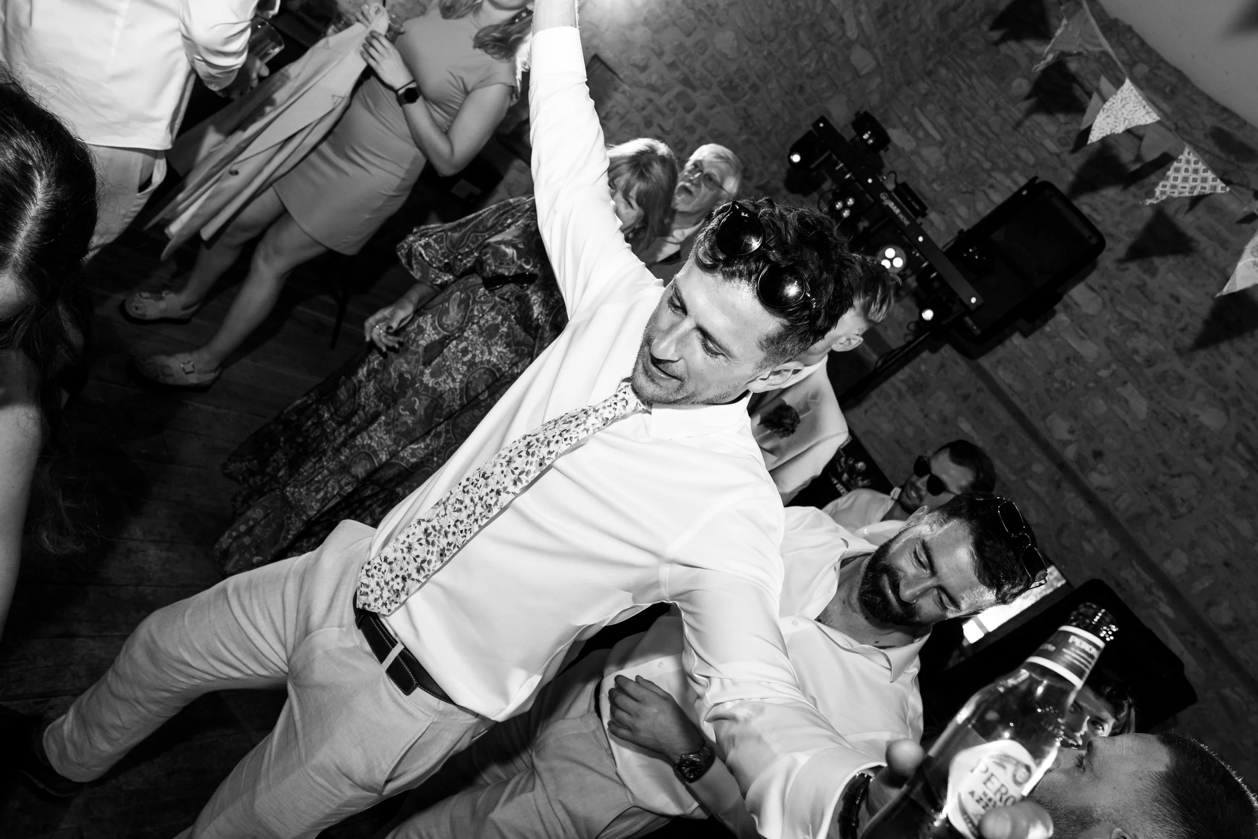People dancing and socializing at a party with drinks, in a room with brick walls and posters.