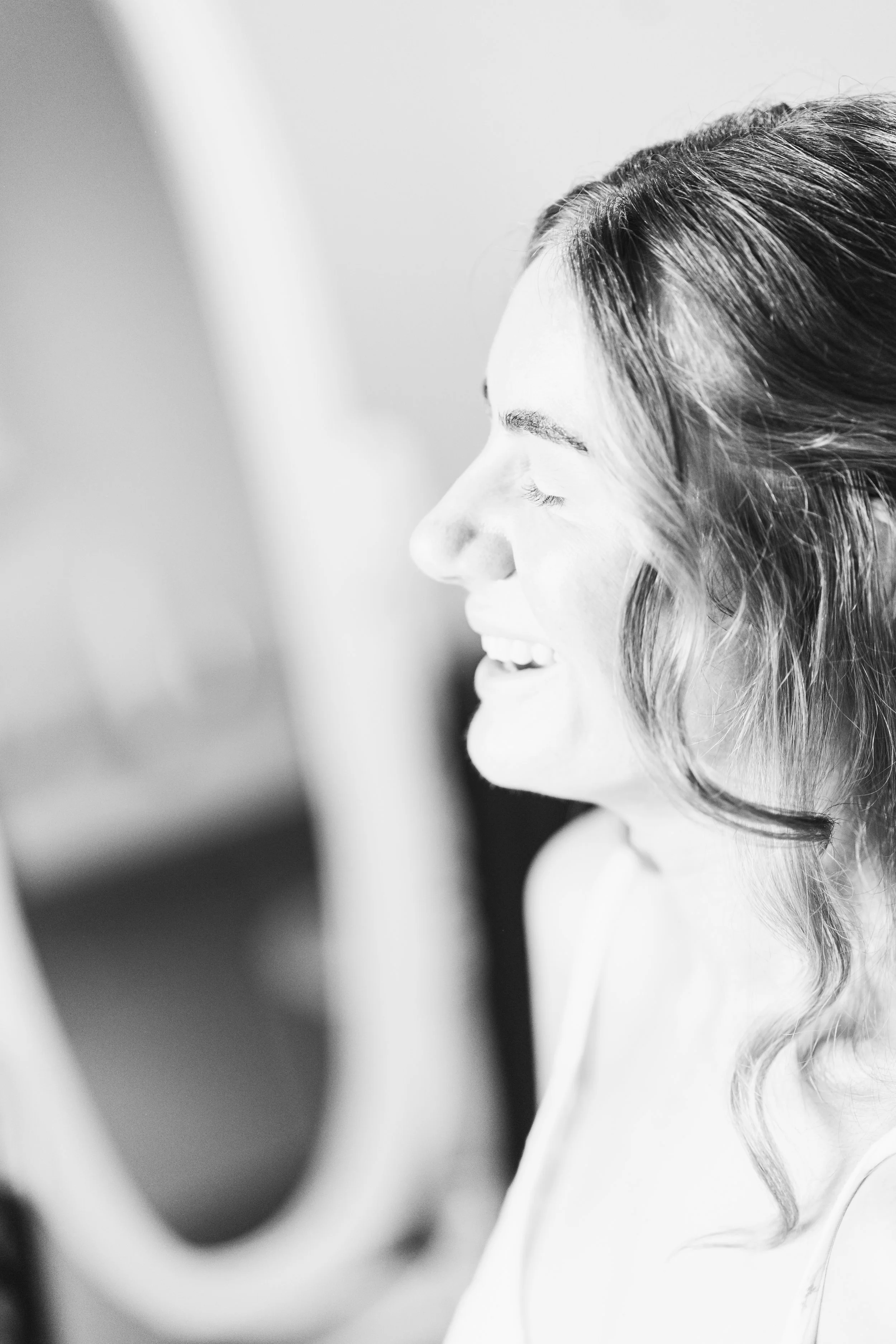Close-up black and white photo of a woman with wavy hair smiling, with her eyes closed, facing to the right.