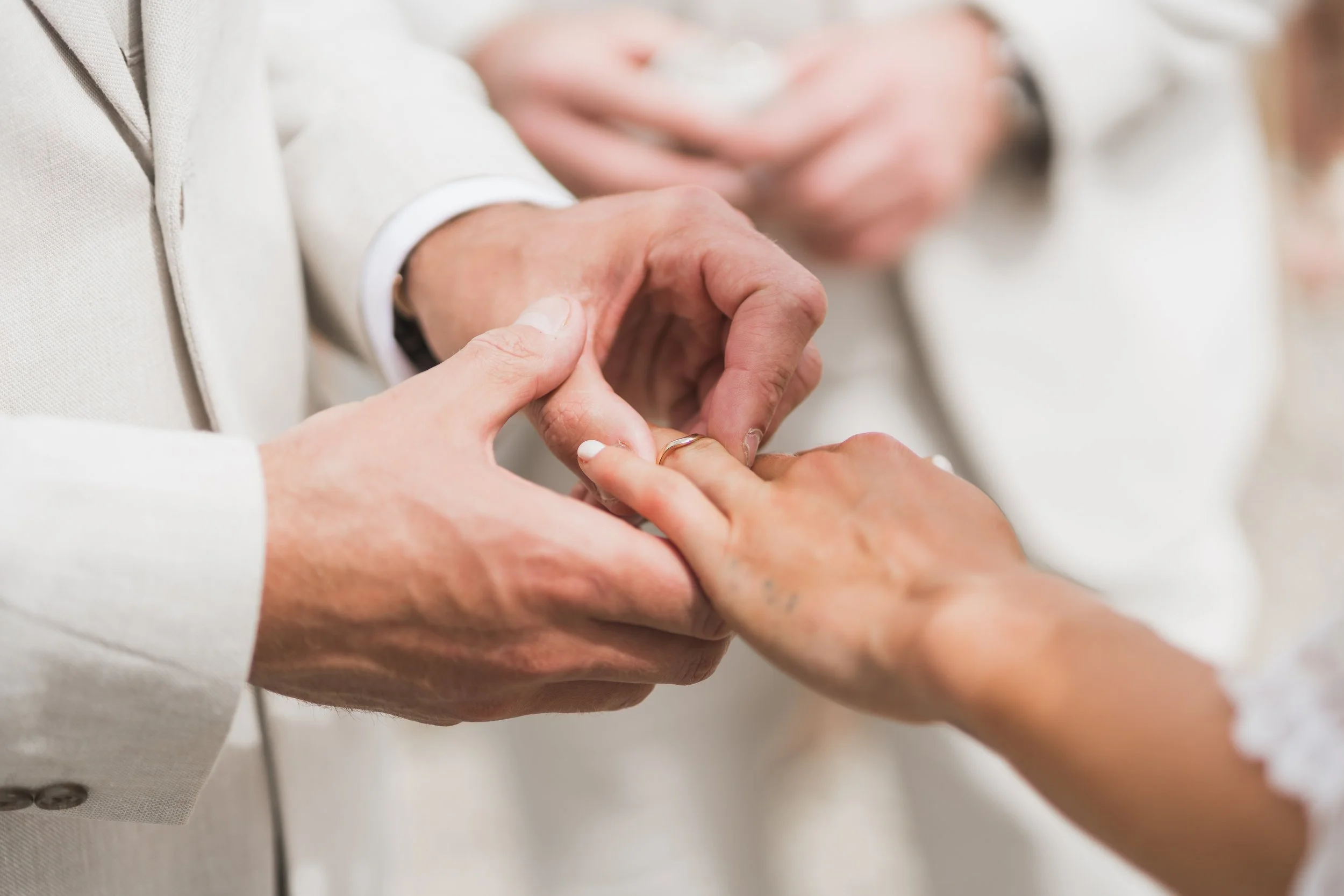 Two people holding hands, showing a romantic gesture, with one person wearing a wedding band.