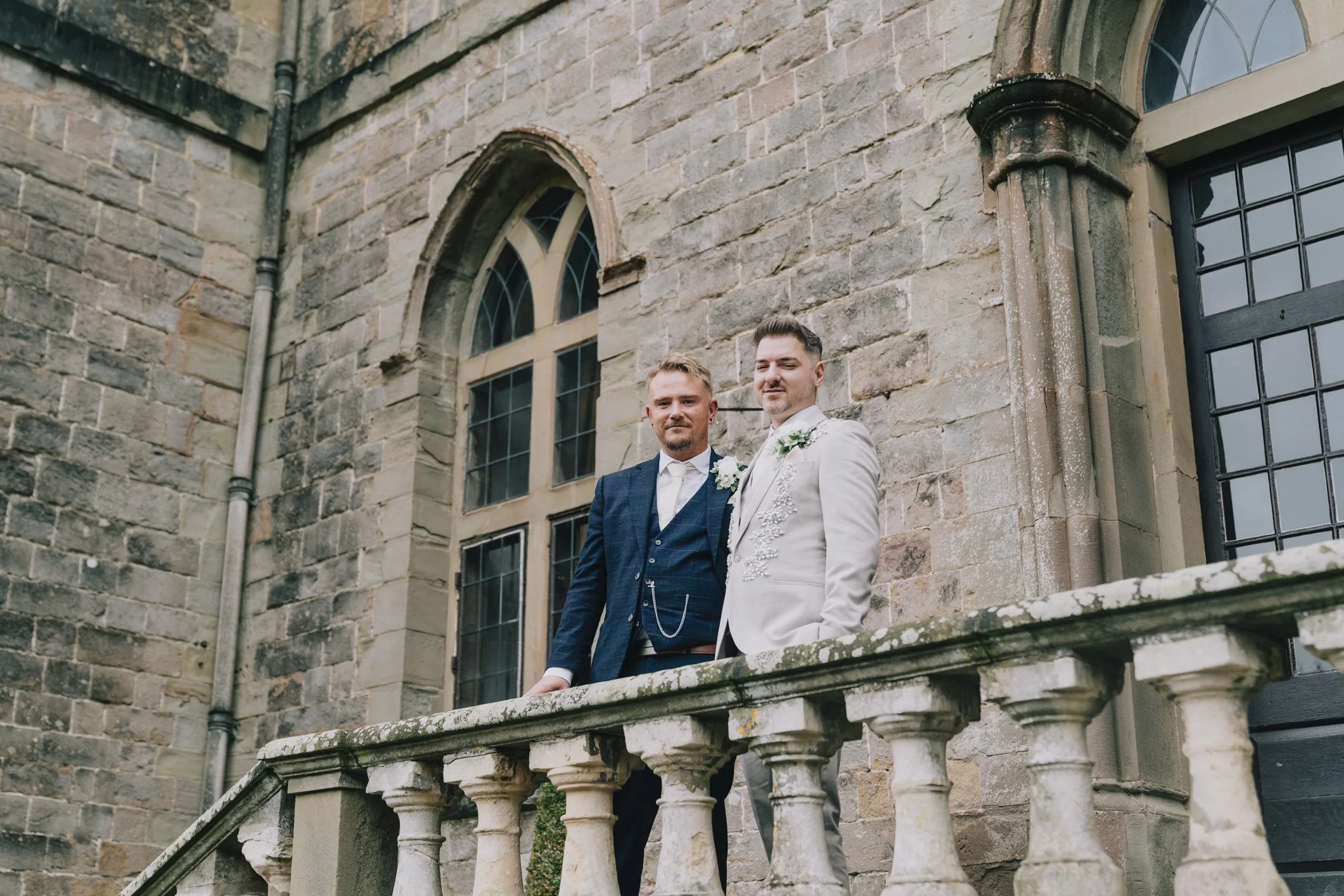 Both grooms smile whilst holding eachother during couple portraits at Clearwell Castle
