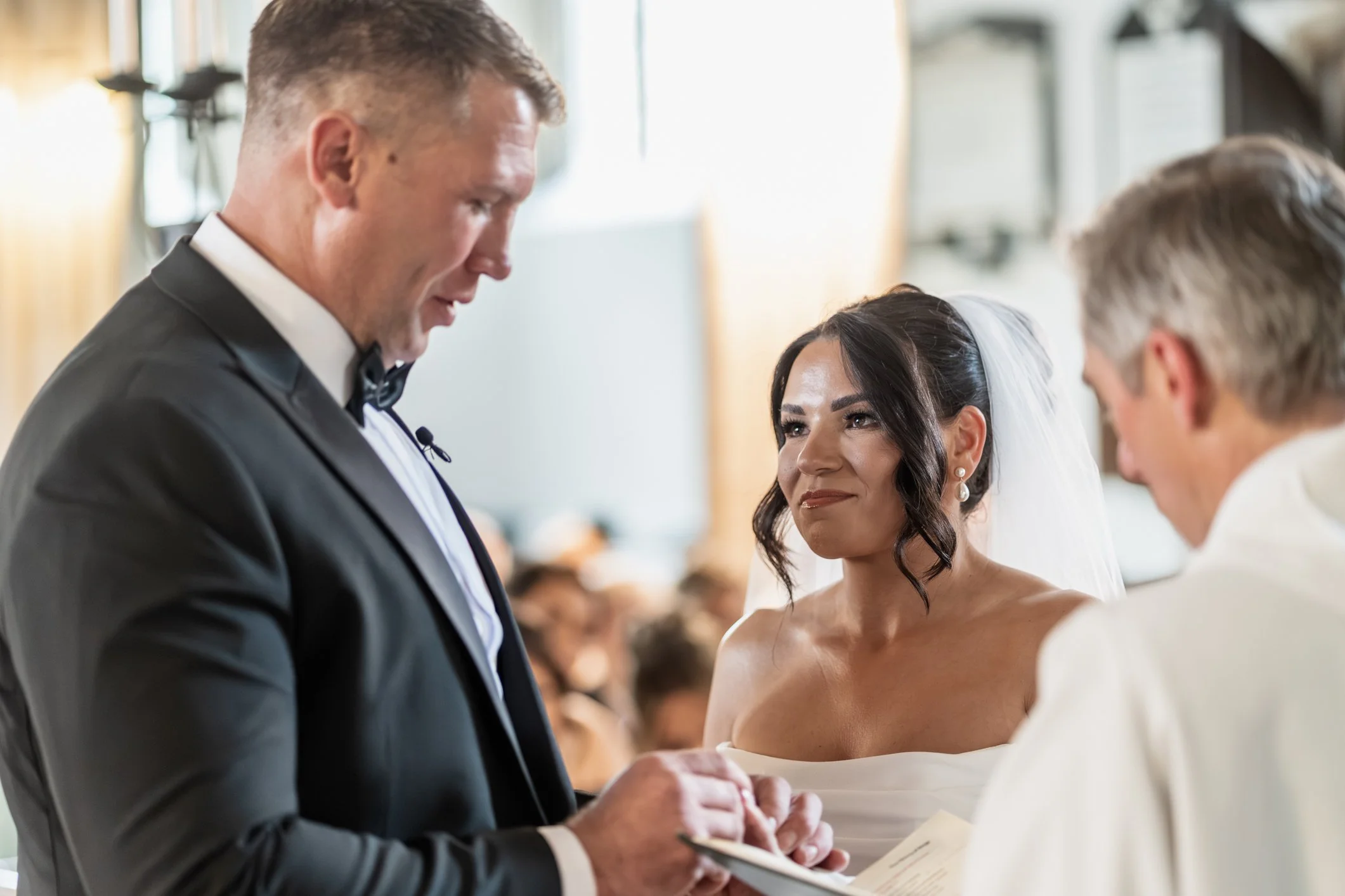 Bride smiling as groom put brides wedding ring on her hand