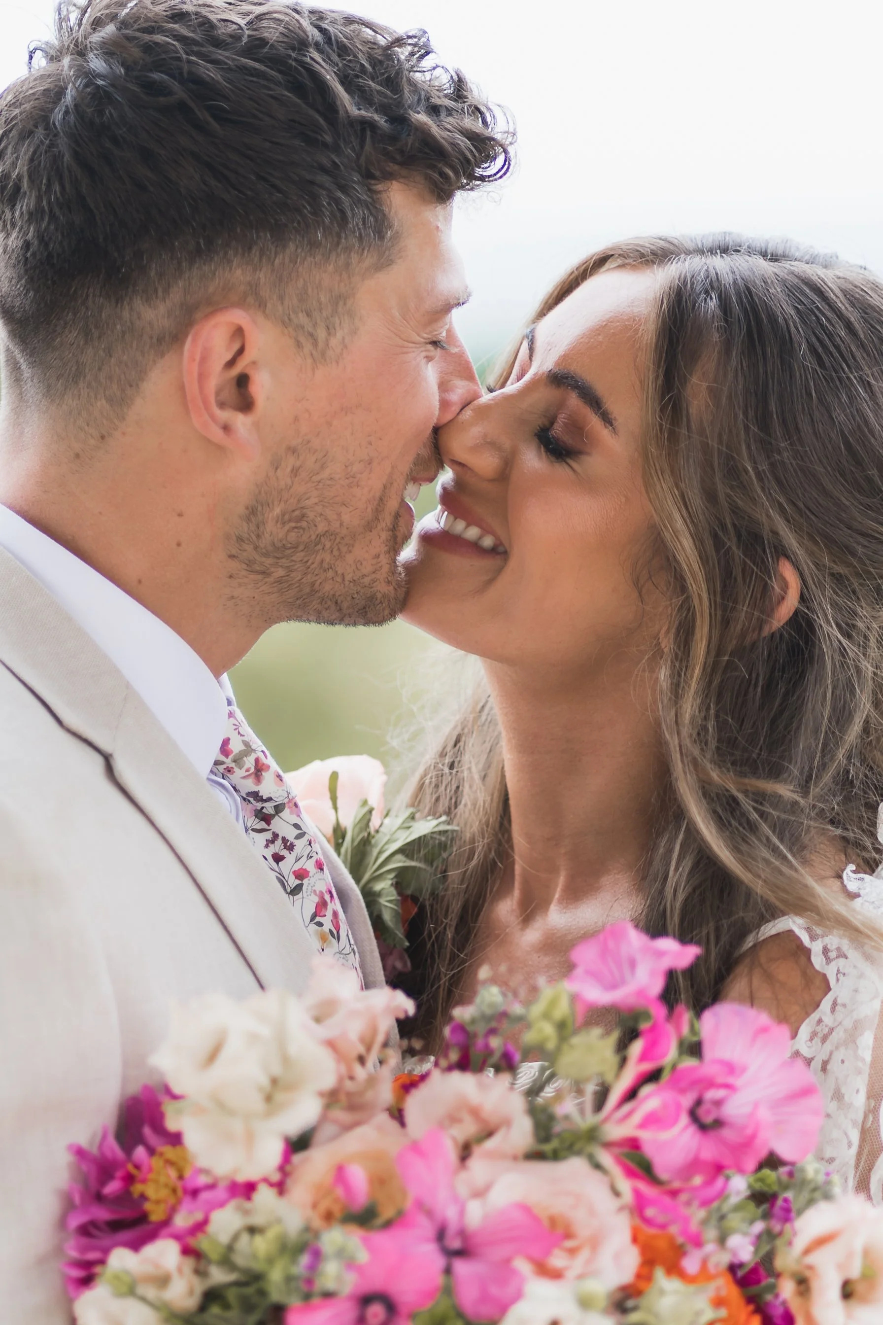 A man and woman are very close, about to kiss, with eyes closed, surrounded by pink, purple, and white flowers.
