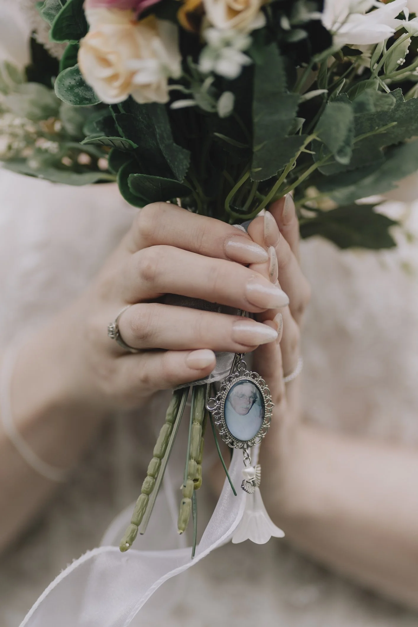 A bride holding a bouquet of flowers with an oval-shaped locket pendant giving memory of her nan attached to the bouquet.