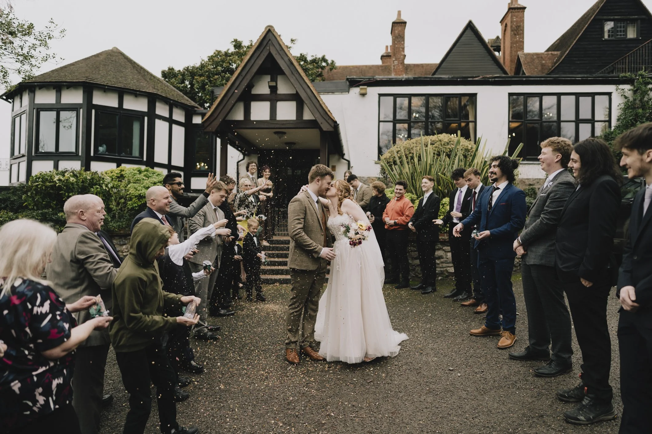 Wedding couple kissing outside a Webbington Hotel and Spa, surrounded by wedding guests throwing rice or confetti.