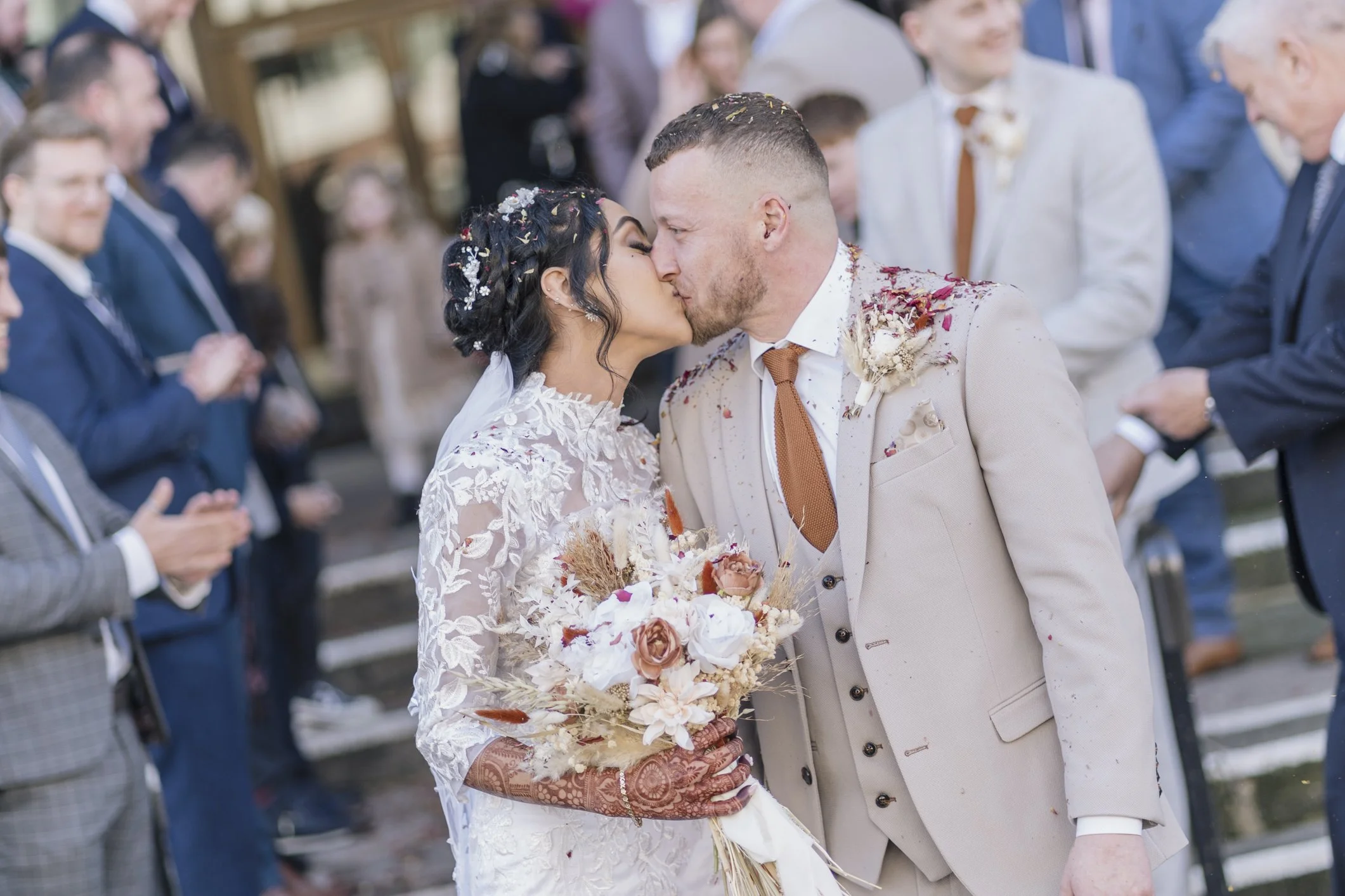 A bride and groom kiss after their wedding ceremony, surrounded by guests on steps outside at Shire Hall in Gloucester