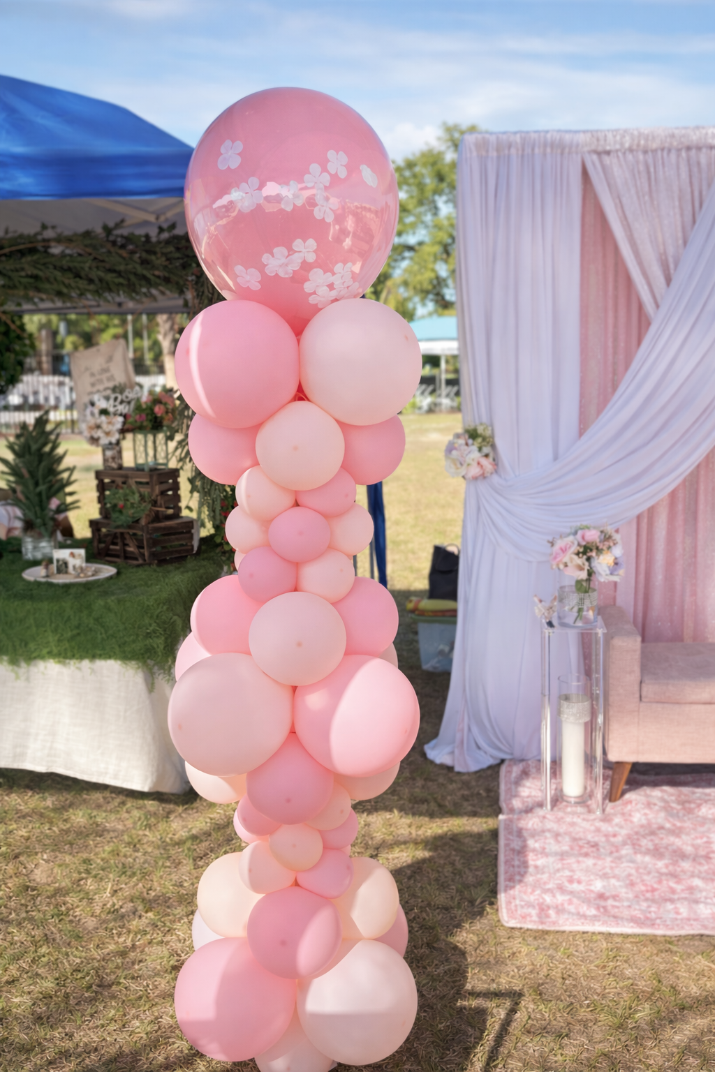 Pink and white balloons in a tall cluster at an outdoor event, with decorated tent area in the background.