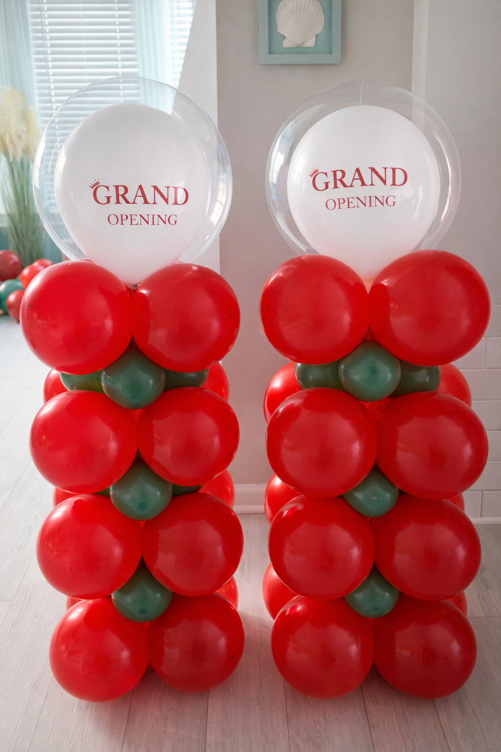 Two balloon pillars with red and green balloons topped with clear balloons that have 'Grand Opening' written in red.