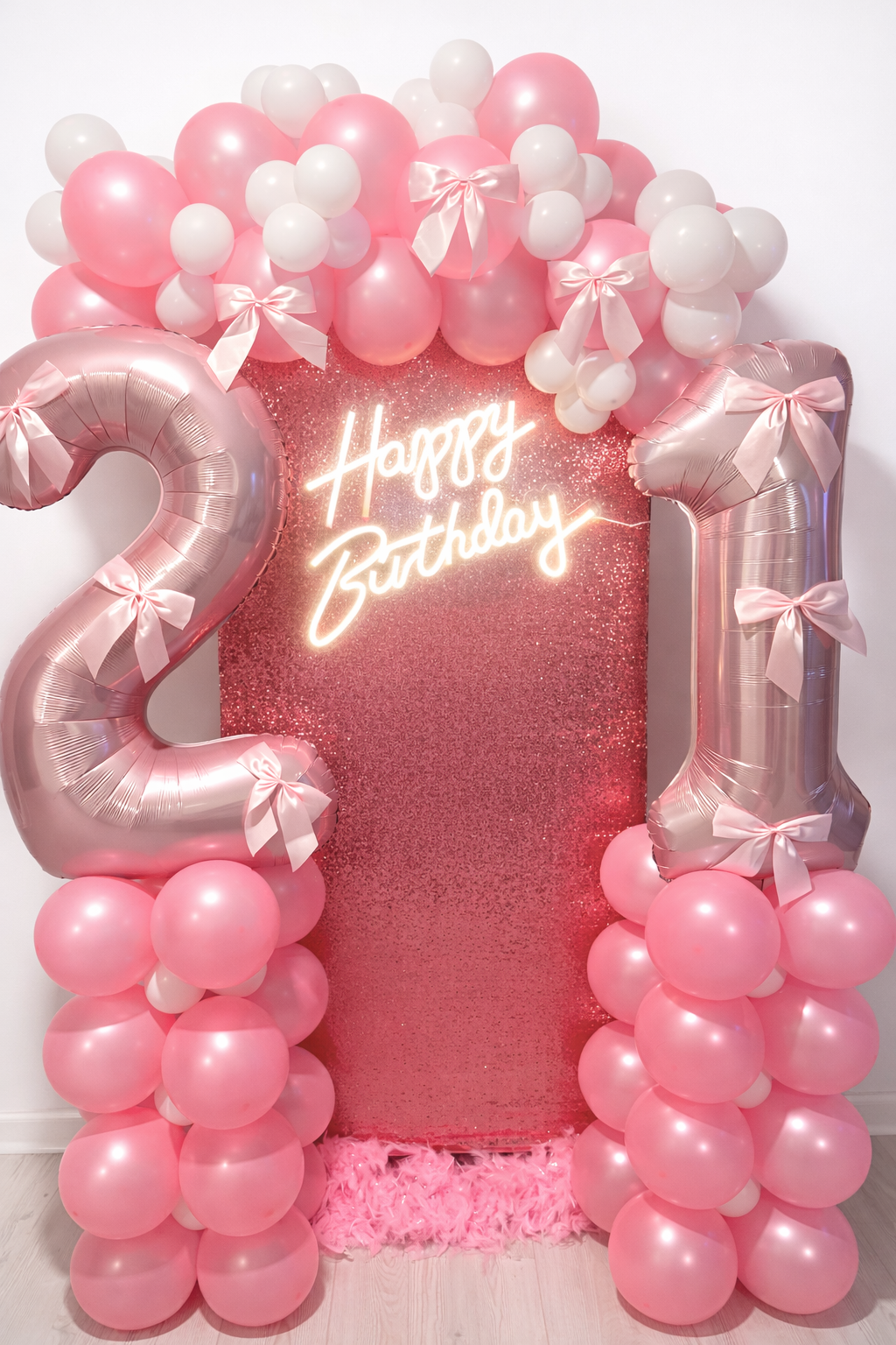 Pink and white balloon arch with two large pink number 2 and 1 balloons, a glittery pink backdrop, and a neon sign that reads "Happy Birthday" in cursive, celebrating a 21st birthday.