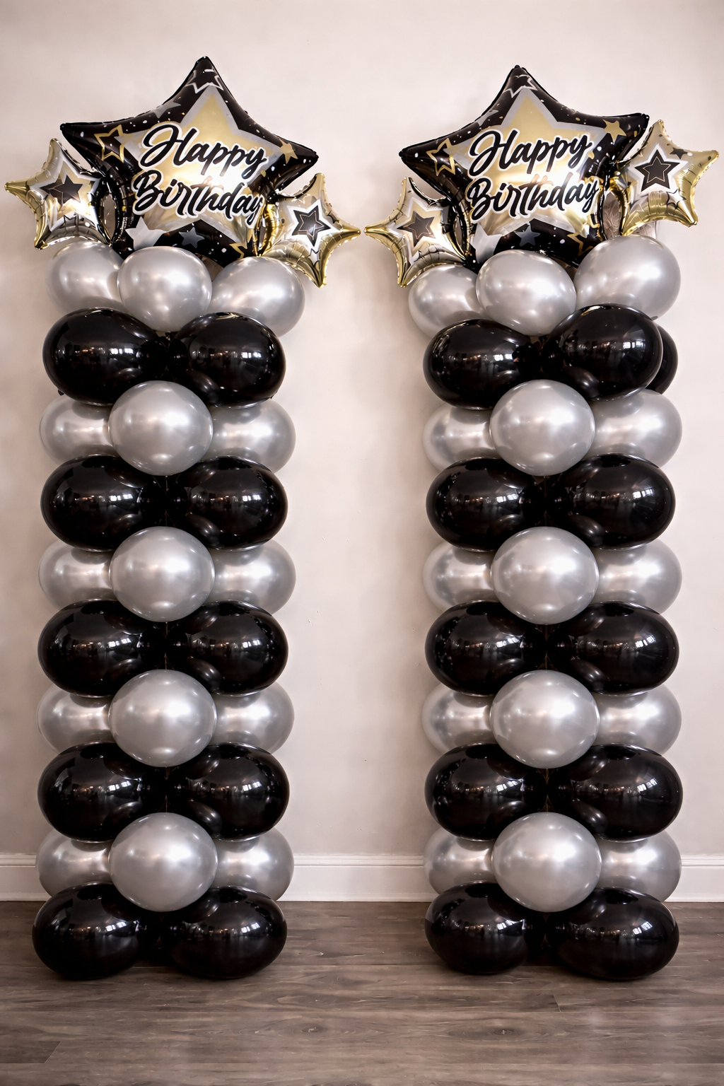 Two balloon columns decorated with black, silver, and gold balloons, topped with star-shaped balloons that say 'Happy Birthday'.