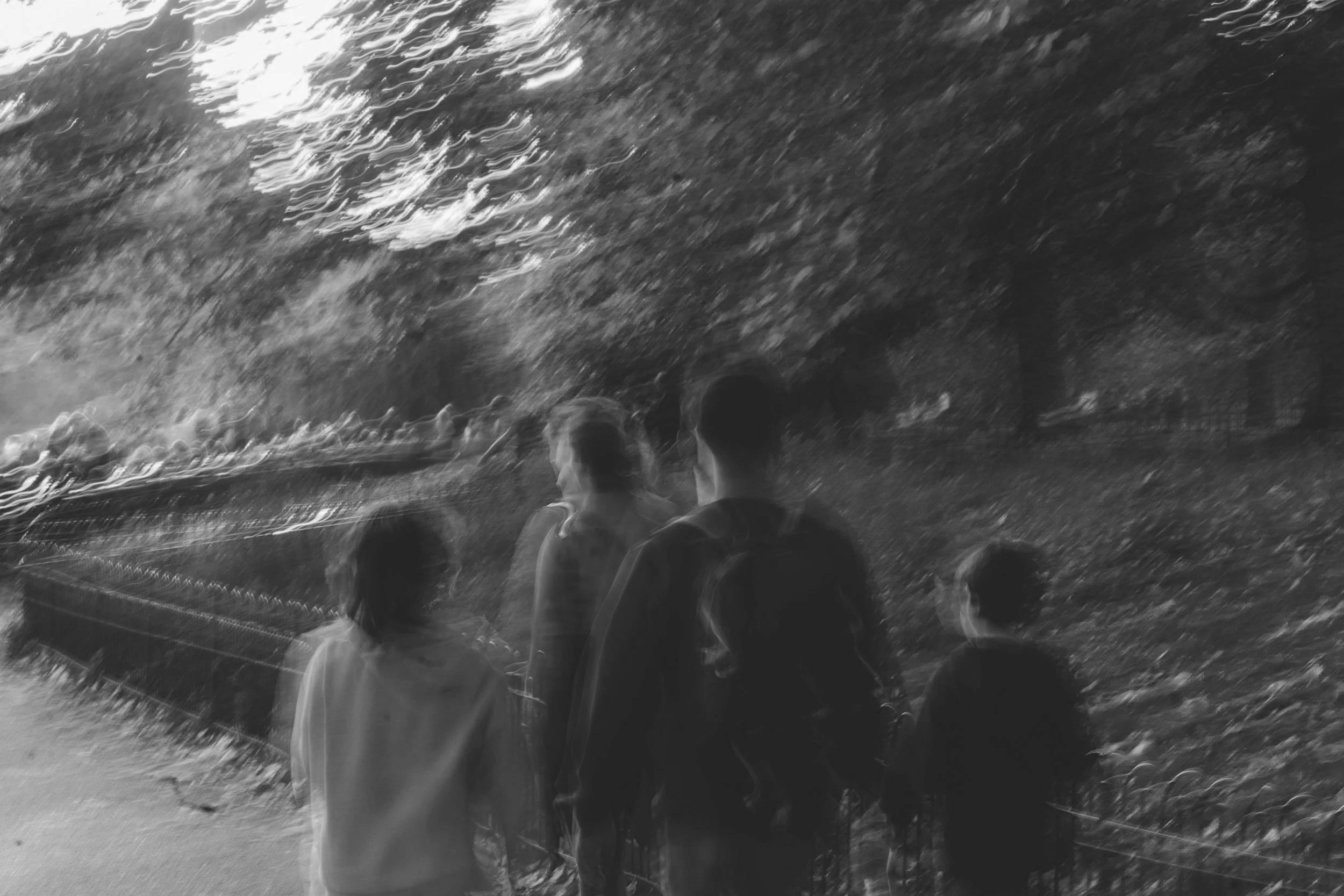 Four people, likely a family, standing near a waterfall in a park or natural area, viewing the water.