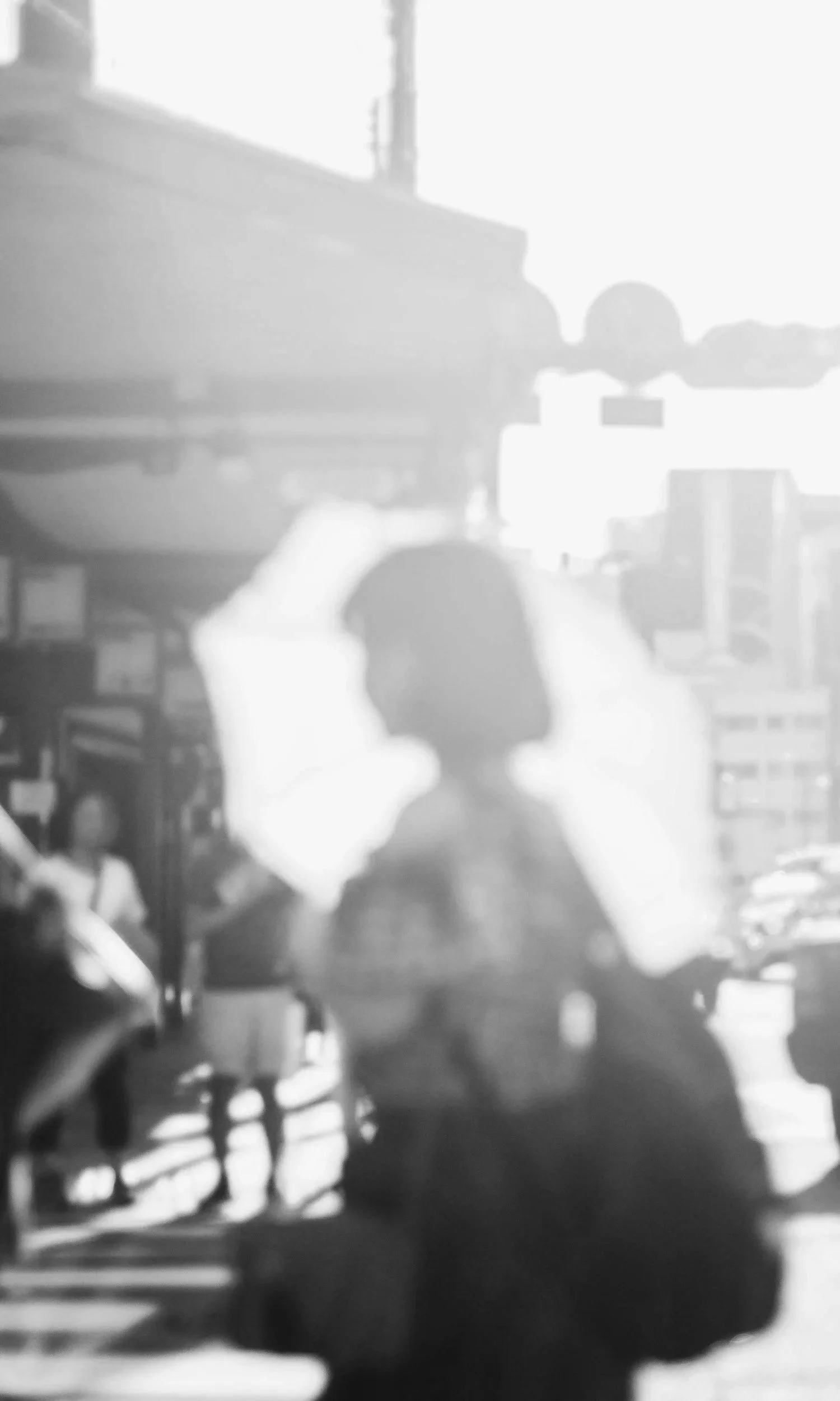 Silhouette of a woman on a city street with buildings and a traffic light in the background, overexposed with high contrast.