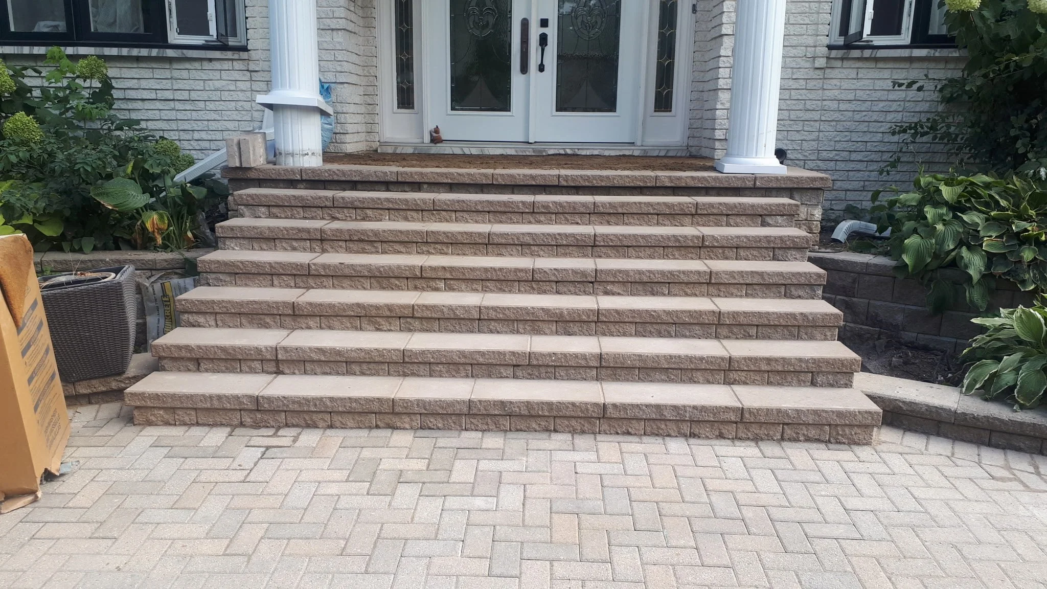 Front entrance with stone steps and pavers leading up to a white door with glass panels, flanked by white columns, greenery on both sides.