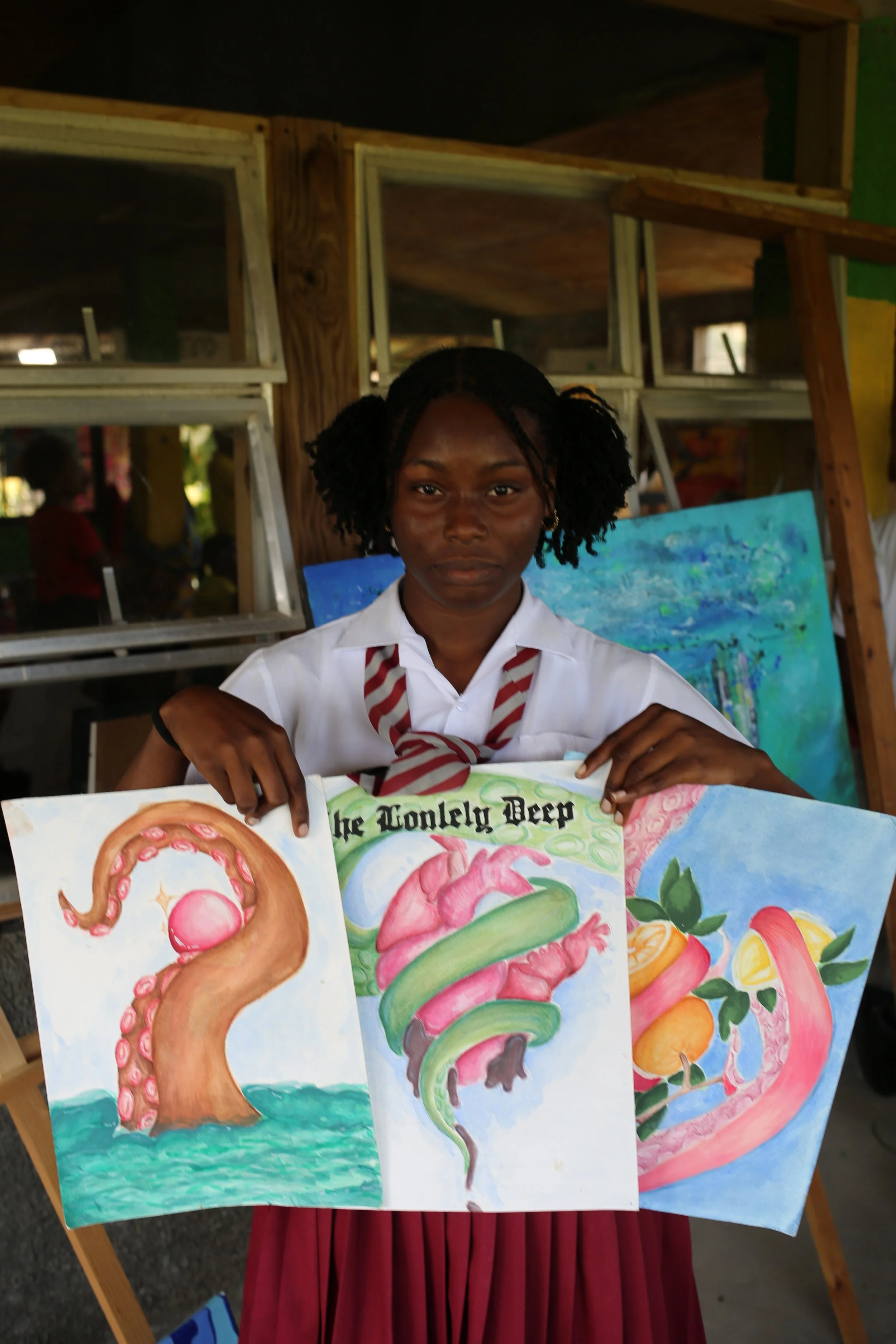 A girl in a white school uniform with a red and white striped tie, standing in front of a wooden display, holds up colorful science-themed posters with illustrations of a tentacle, a brain, and a digestive system.