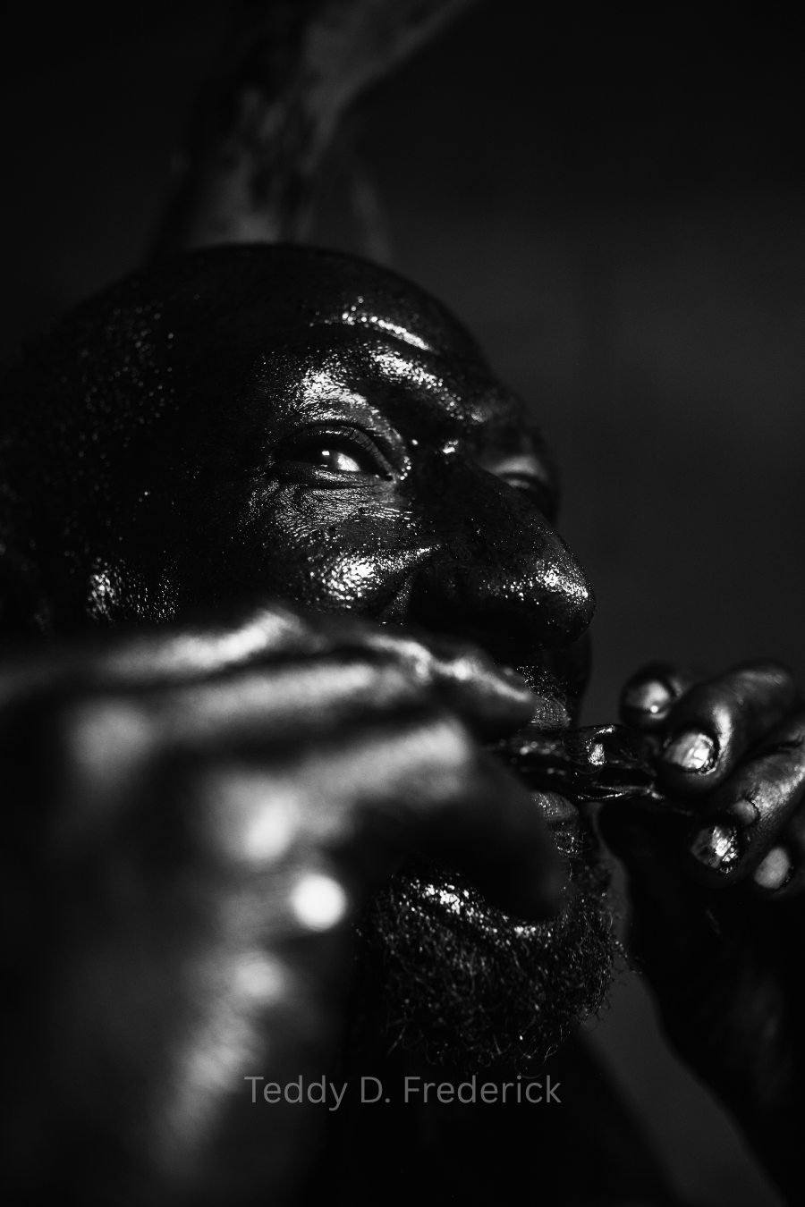 Close-up black and white photo of a person with a beard applying a liquid substance to their lips, with focused expression and hands visible.