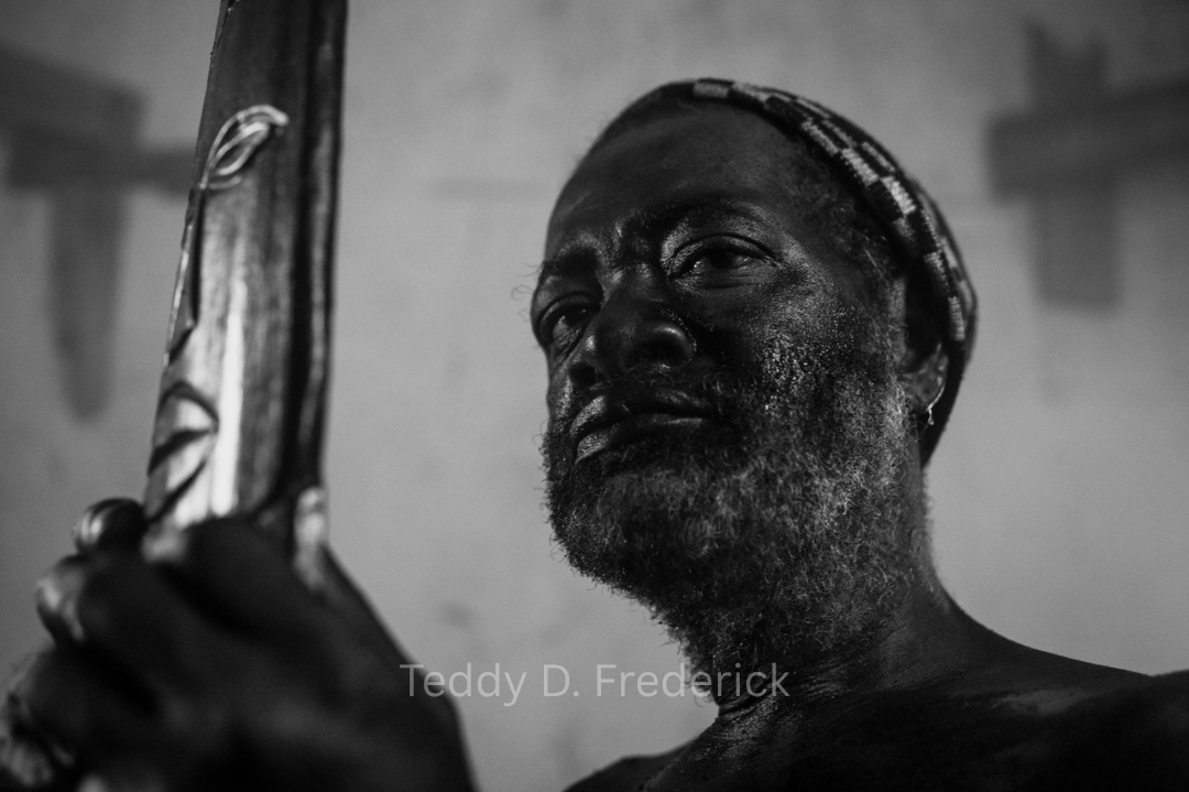 A man with a beard looking at a mirror while holding a phone, with a focused expression