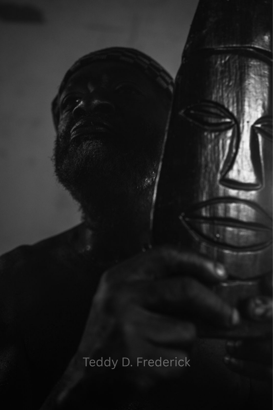 A person holding a Tribal mask made of carved wood, with their face partially obscured by shadows.
