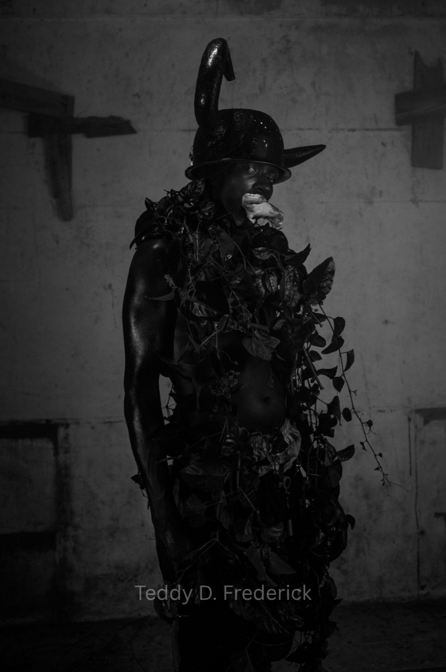 A person dressed in costume, wearing a hat with a horn and surrounded by leaves, is eating a piece of food in a dimly lit room.