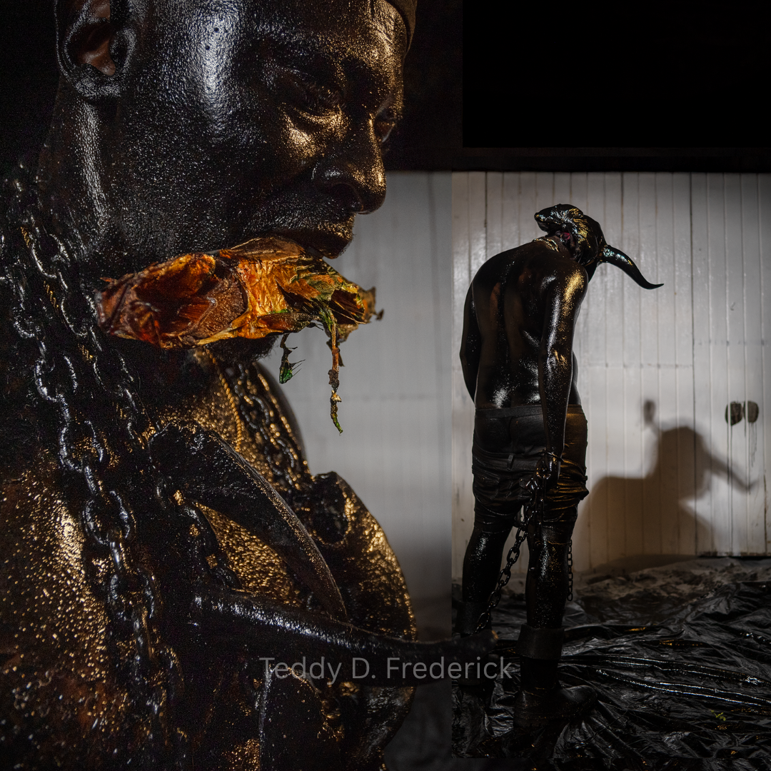 A person with shiny black skin is posed with a large butterfly-shaped leaf around their neck, and they are chained from the wrists. In the background, there is a wall with shadows and a person wearing an animal mask with an elongated snout, also with